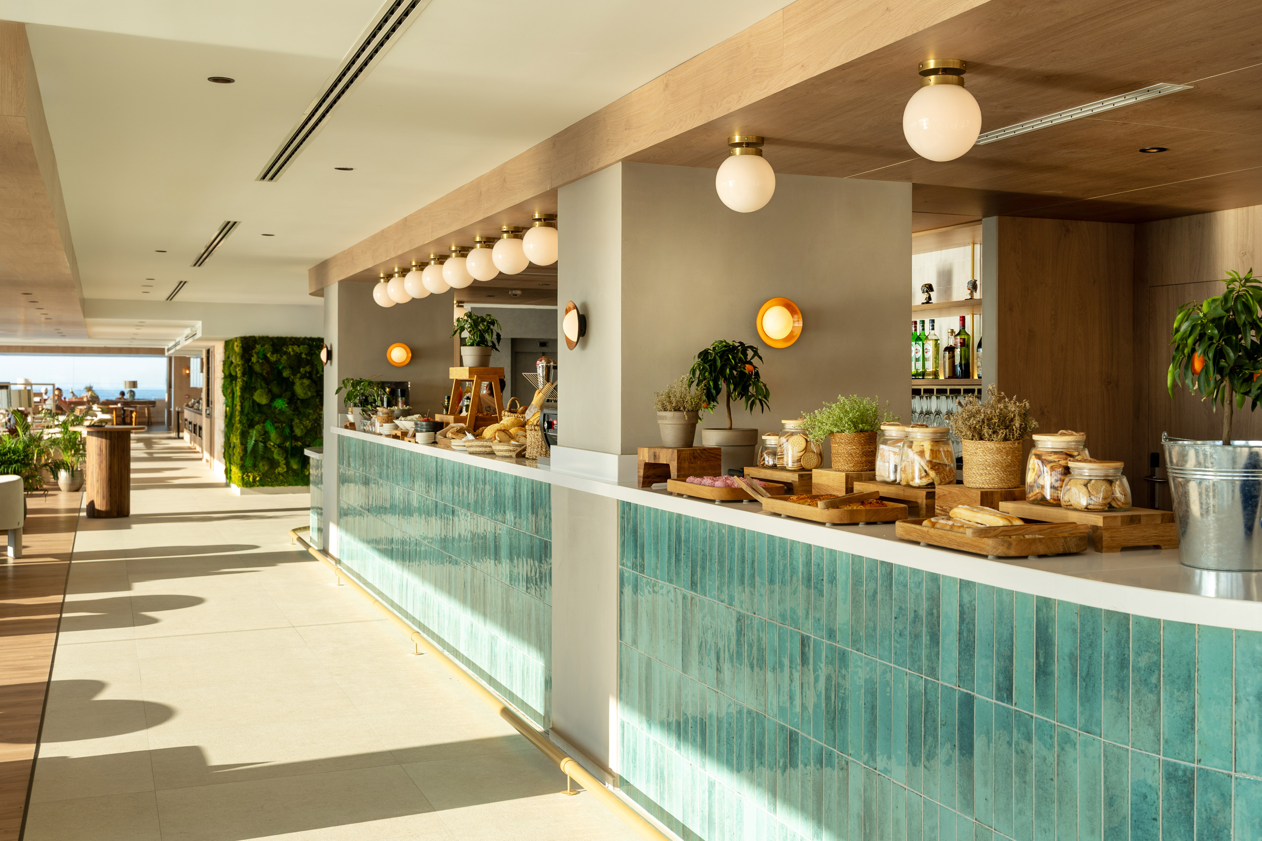 Bright hotel breakfast buffet with turquoise tile bar and food display.
