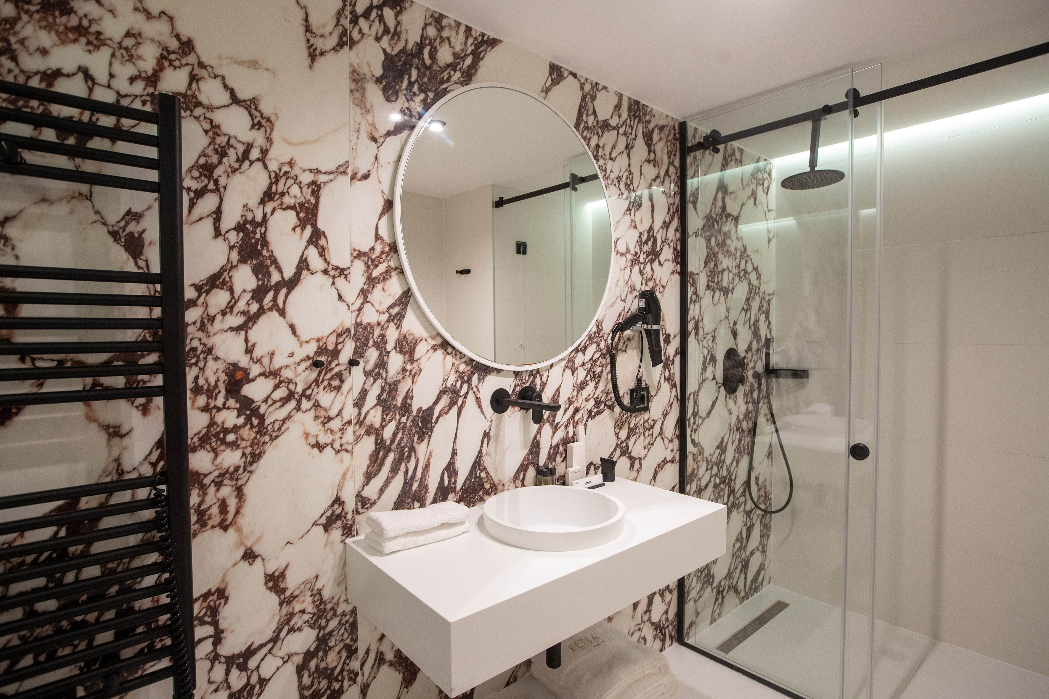 Modern bathroom with marble walls, white vanity, round mirror, and glass shower.