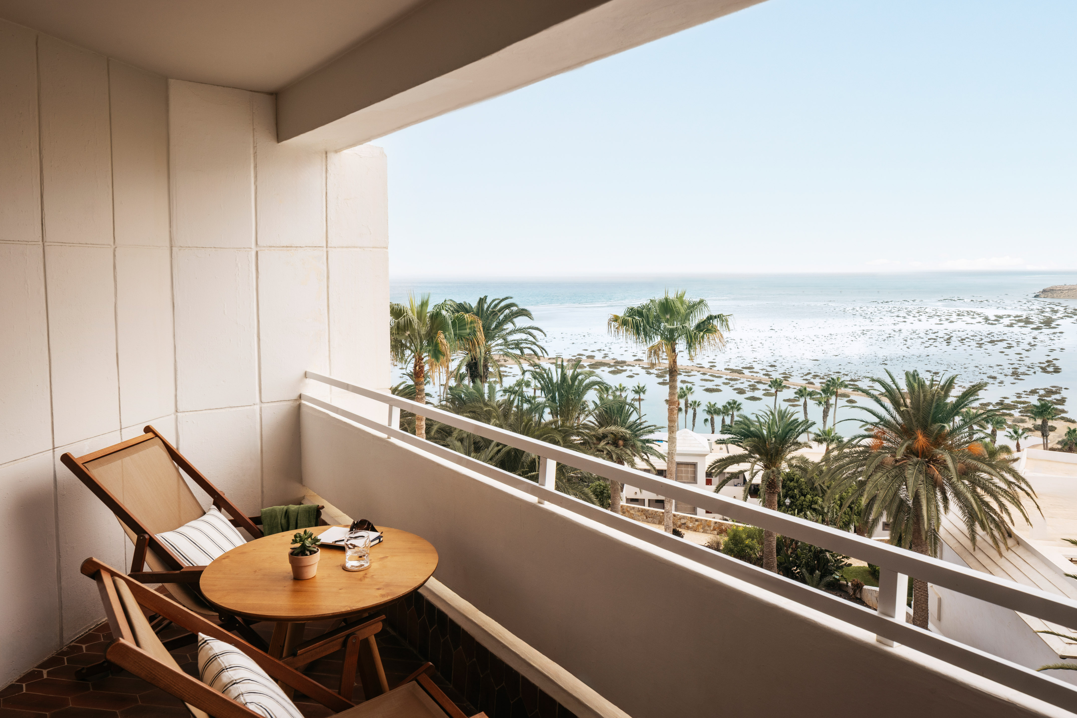 Resort balcony with ocean view, palm trees, and outdoor seating.