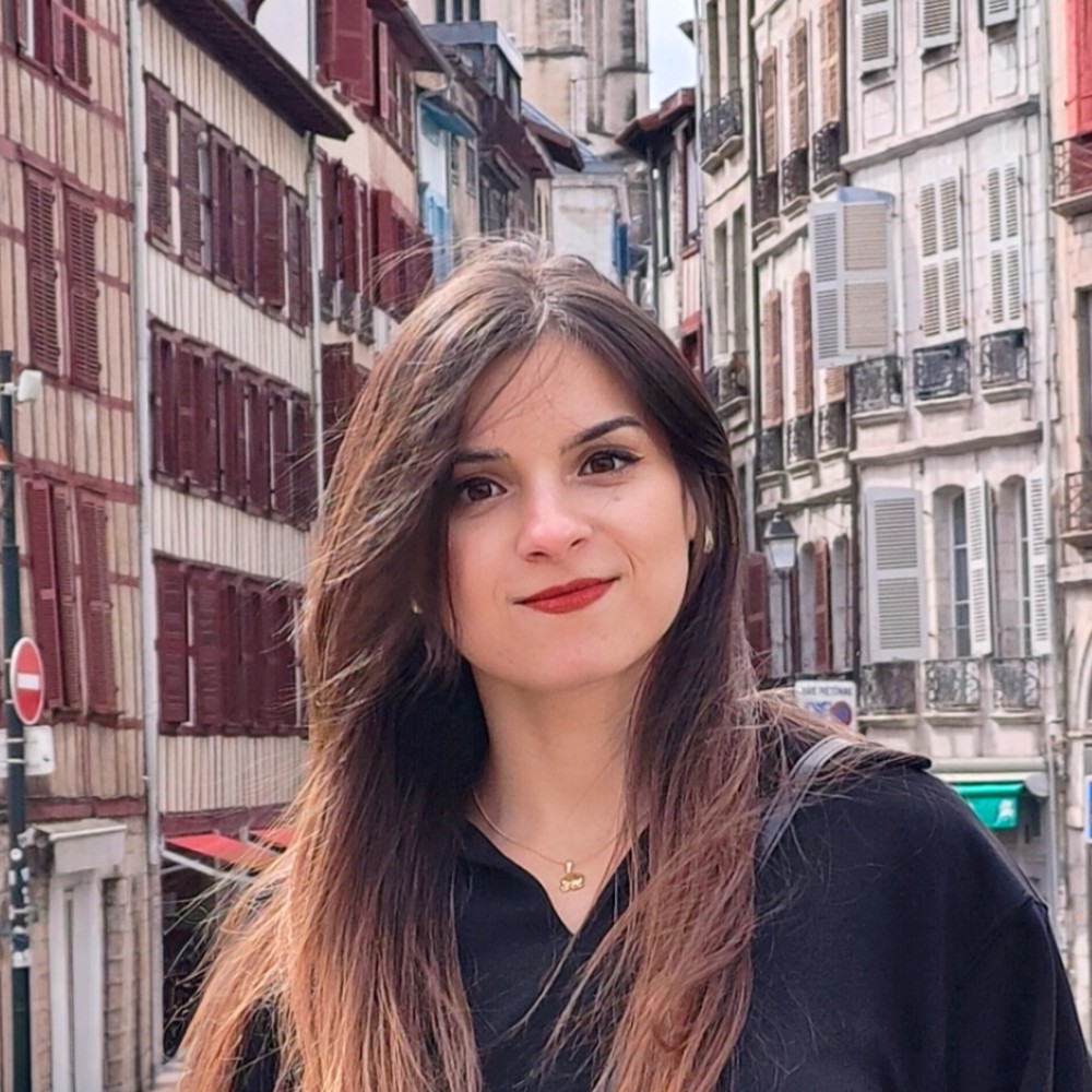 Smiling woman, long hair, red lipstick, traditional European street buildings background.