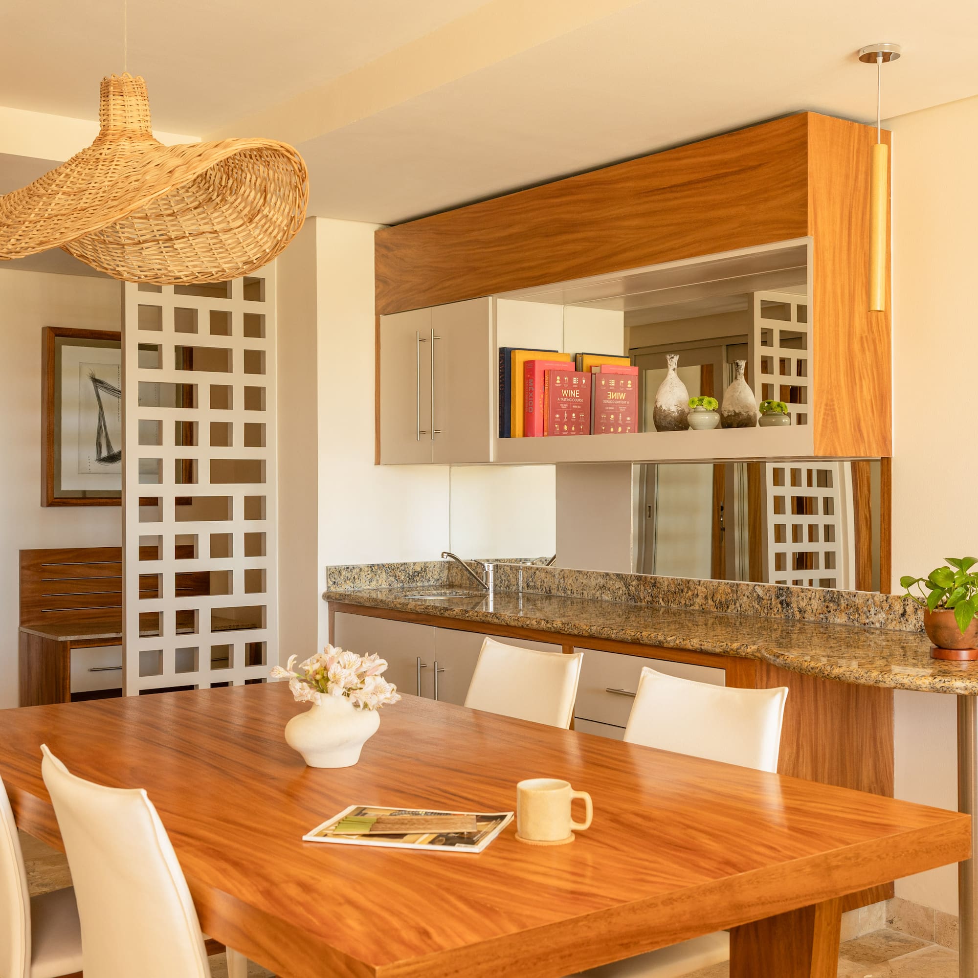 Modern dining room & kitchen with wooden table, white chairs, rattan light.
