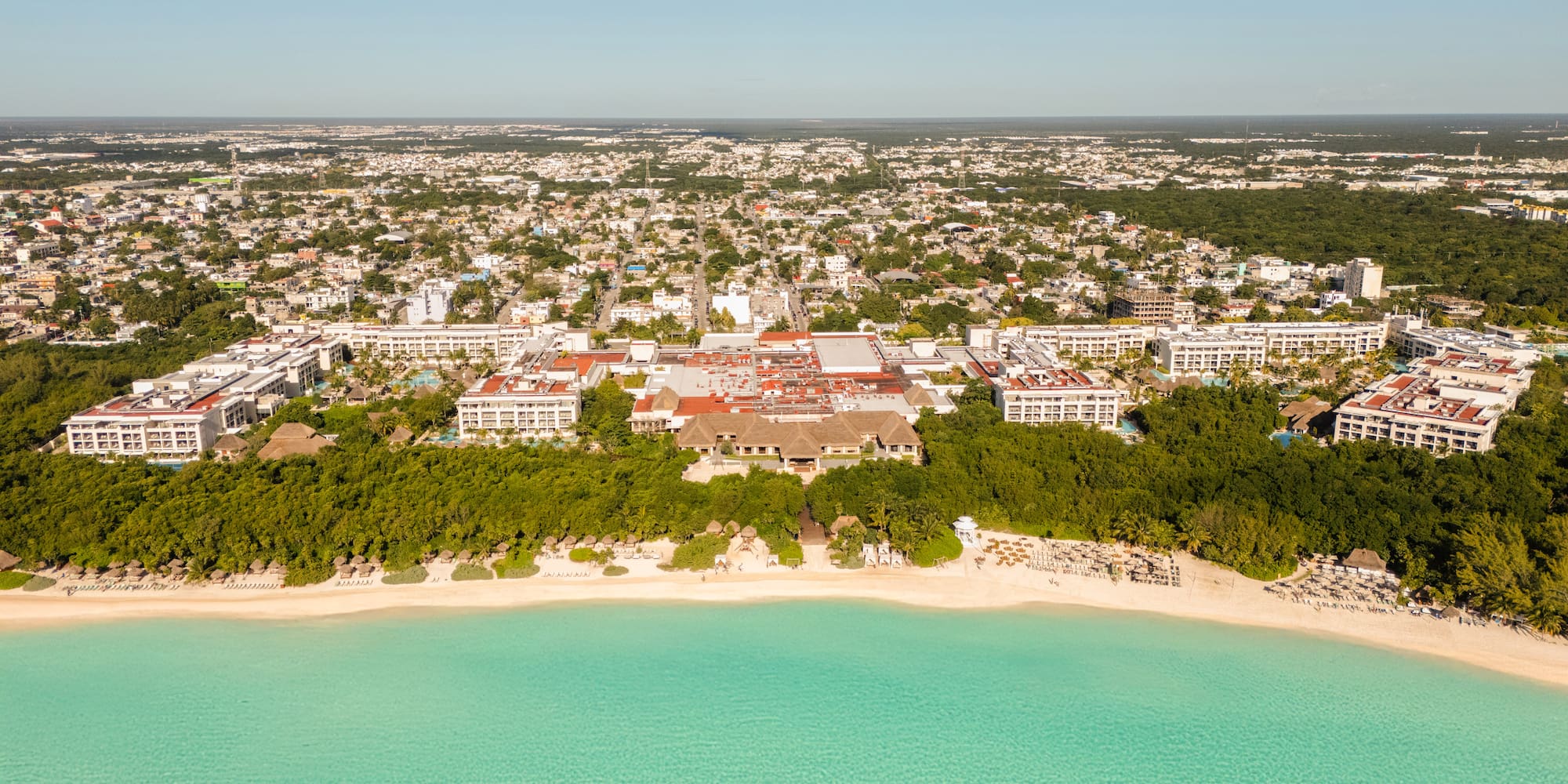 Aerial tropical beach resort, turquoise sea, white sand, coastal city background.