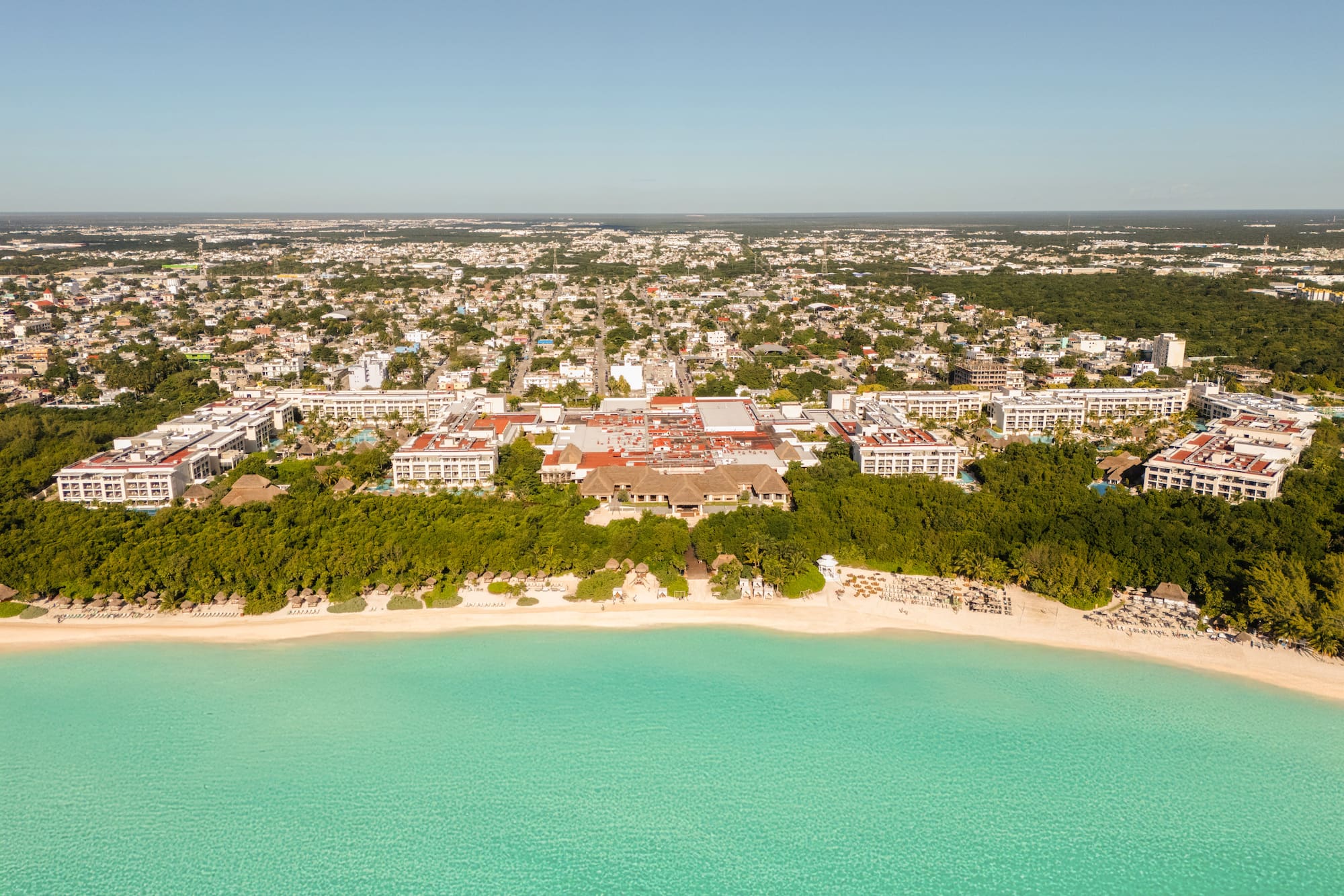 Aerial tropical beach resort, turquoise sea, white sand, coastal city background.