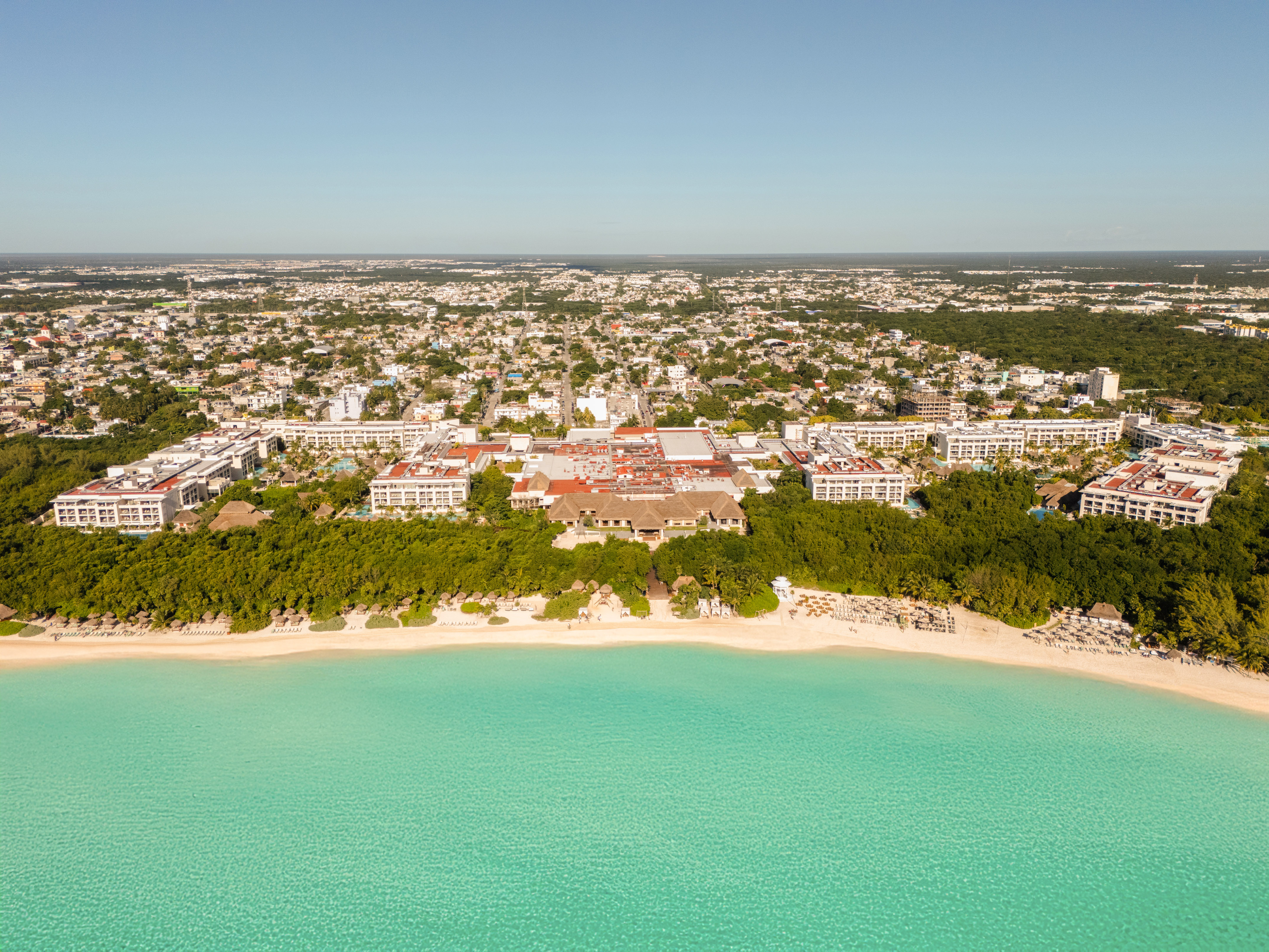 Aerial tropical beach resort, turquoise sea, white sand, coastal city background.