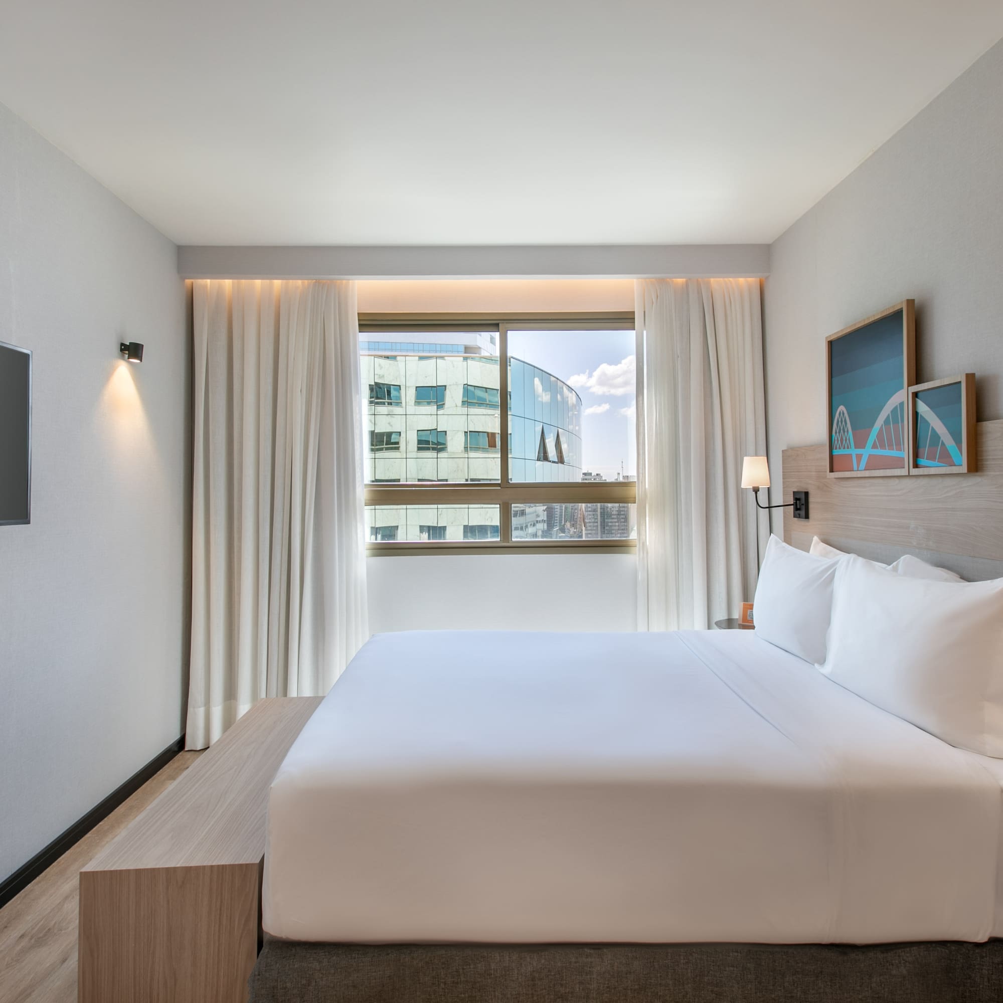 Modern hotel room with king bed, city view window, and wall-mounted TV.
