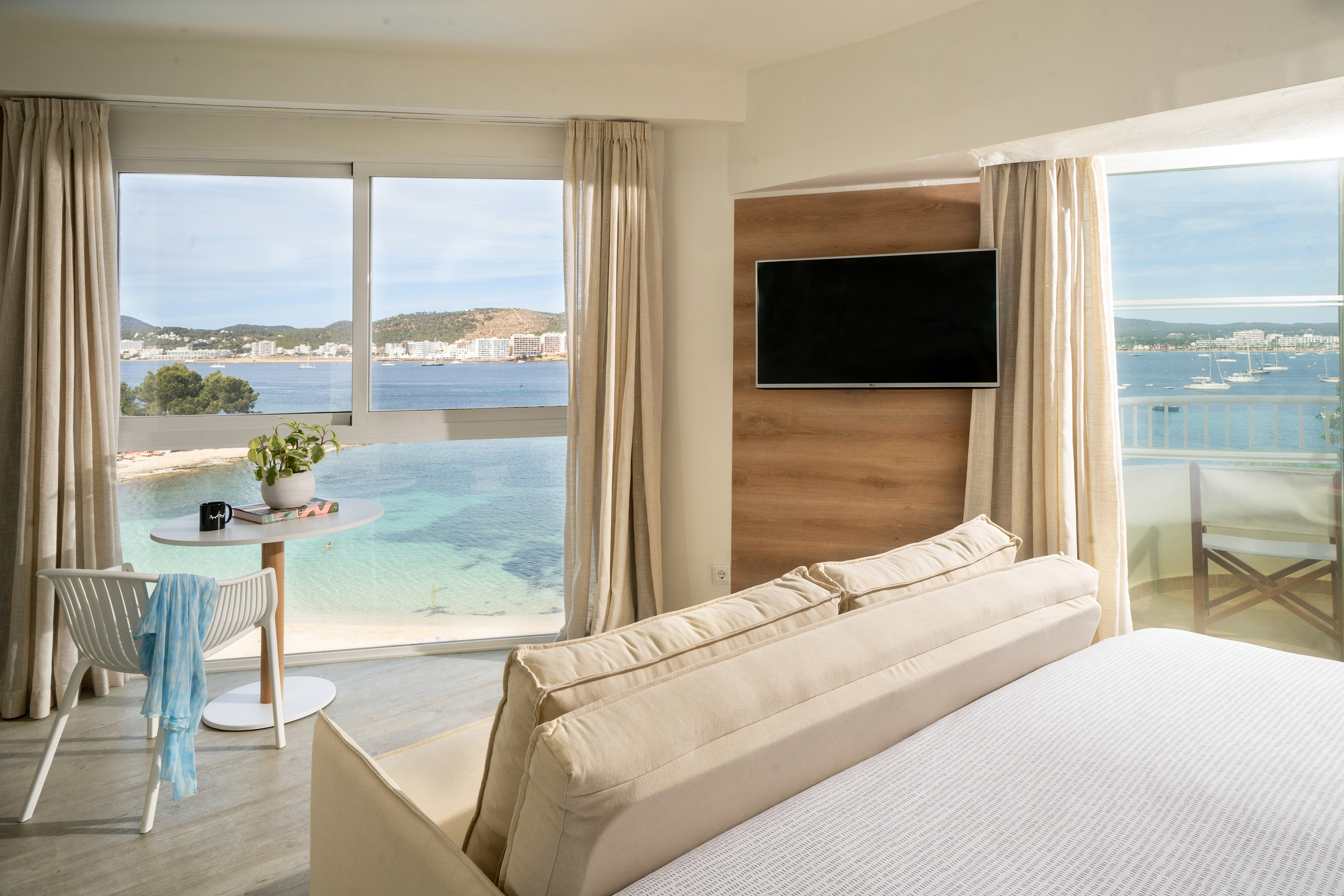 Modern hotel room with sea view, sandy beach, and light contemporary design.