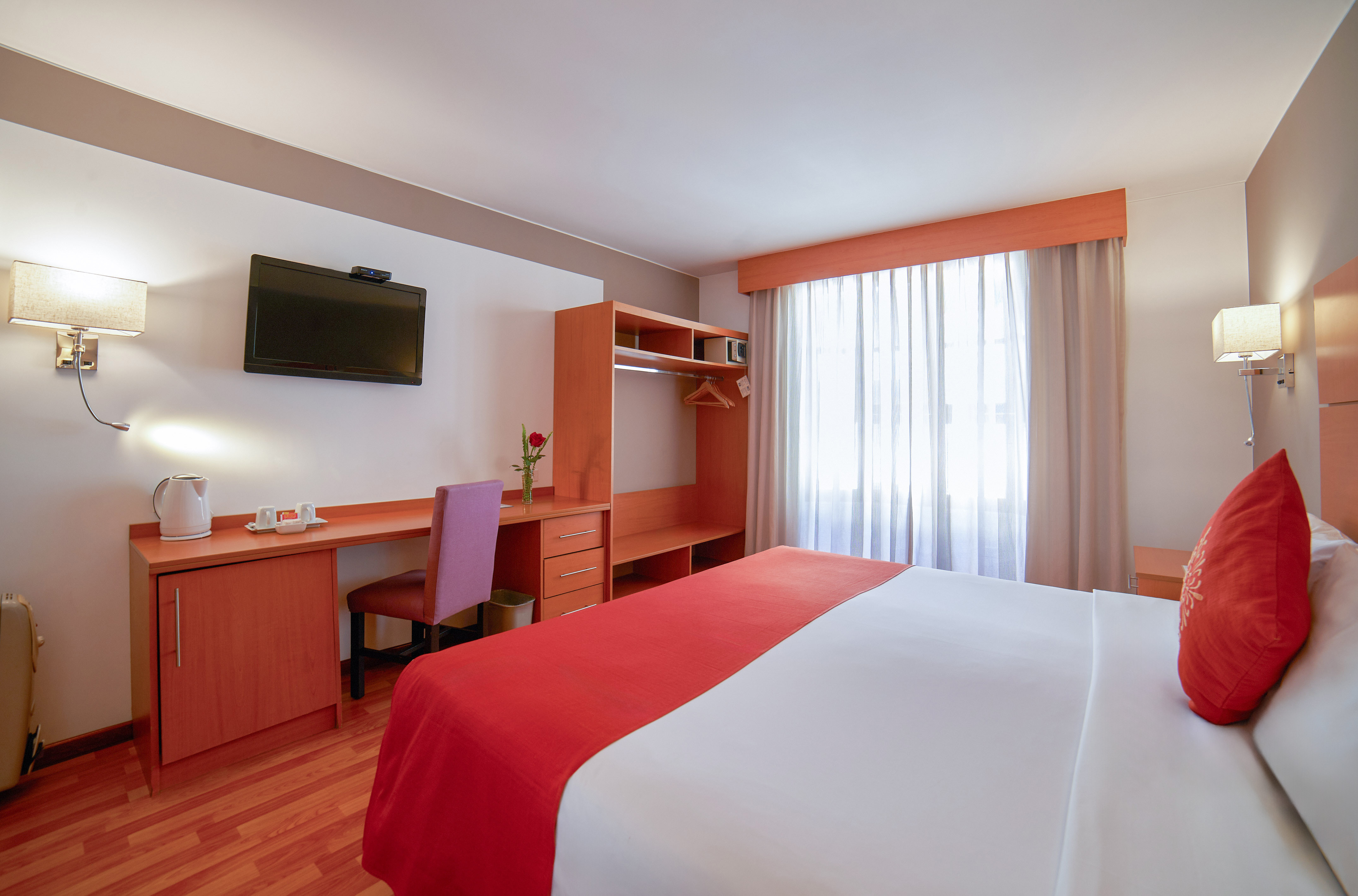 Well-appointed hotel room with bed, desk, TV, and bright window.