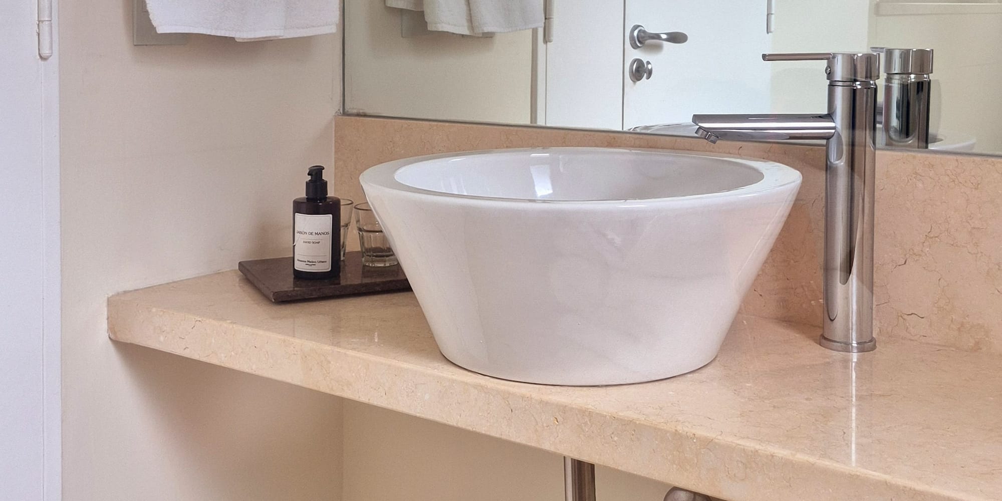 White vessel sink, chrome faucet on marble bathroom vanity.