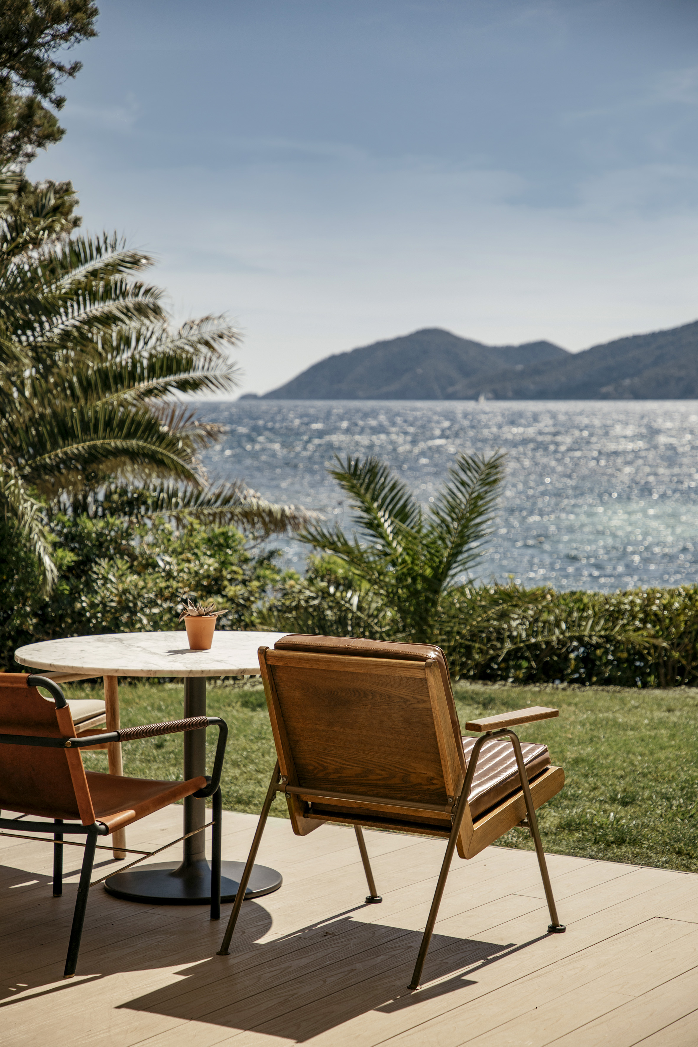 Sunny outdoor patio with table, chairs, and sparkling blue sea view.