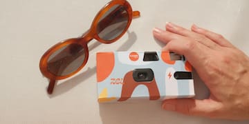 a hand holding a camera and sunglasses