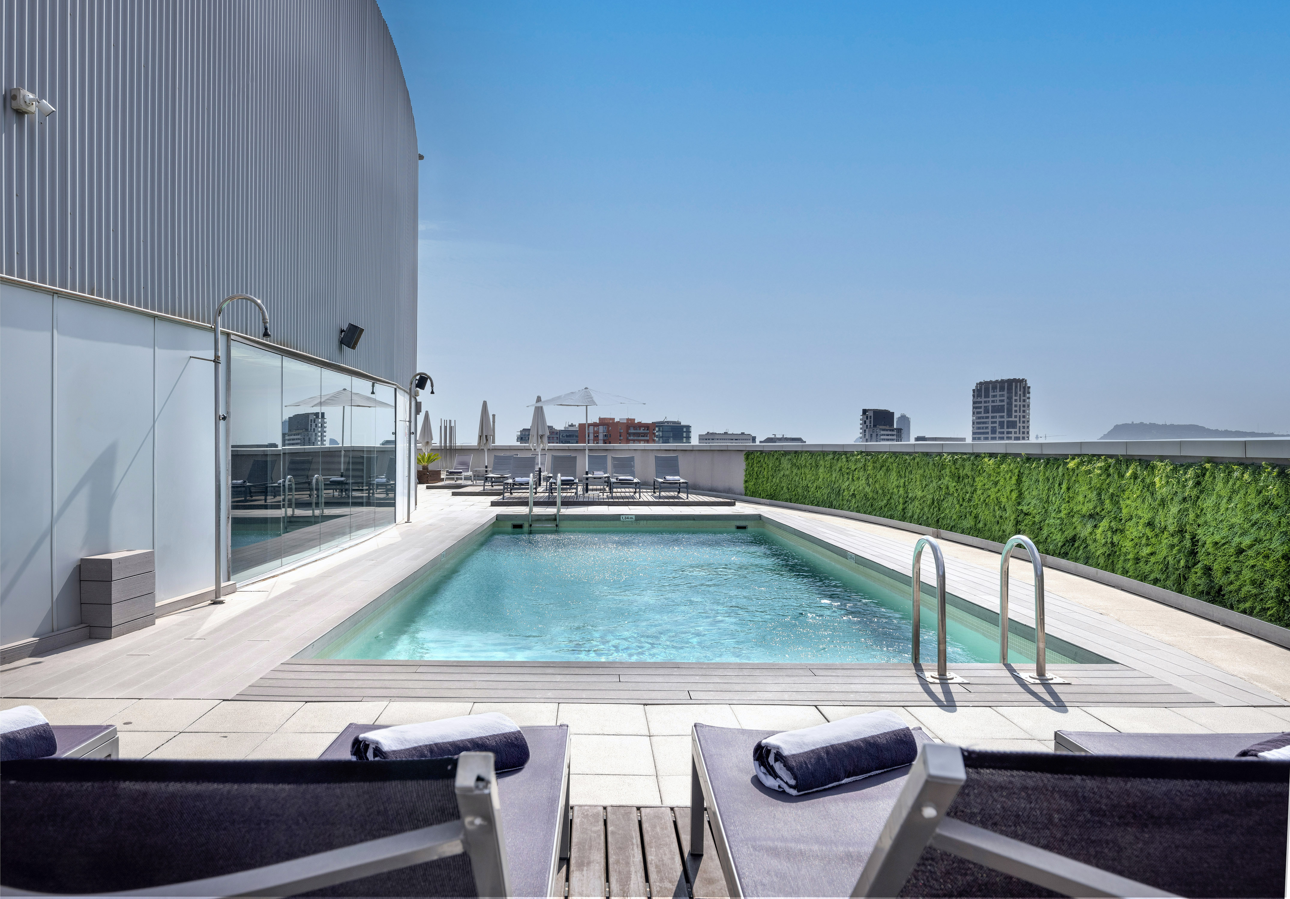 Rooftop hotel swimming pool with lounge chairs, city view, and blue sky.