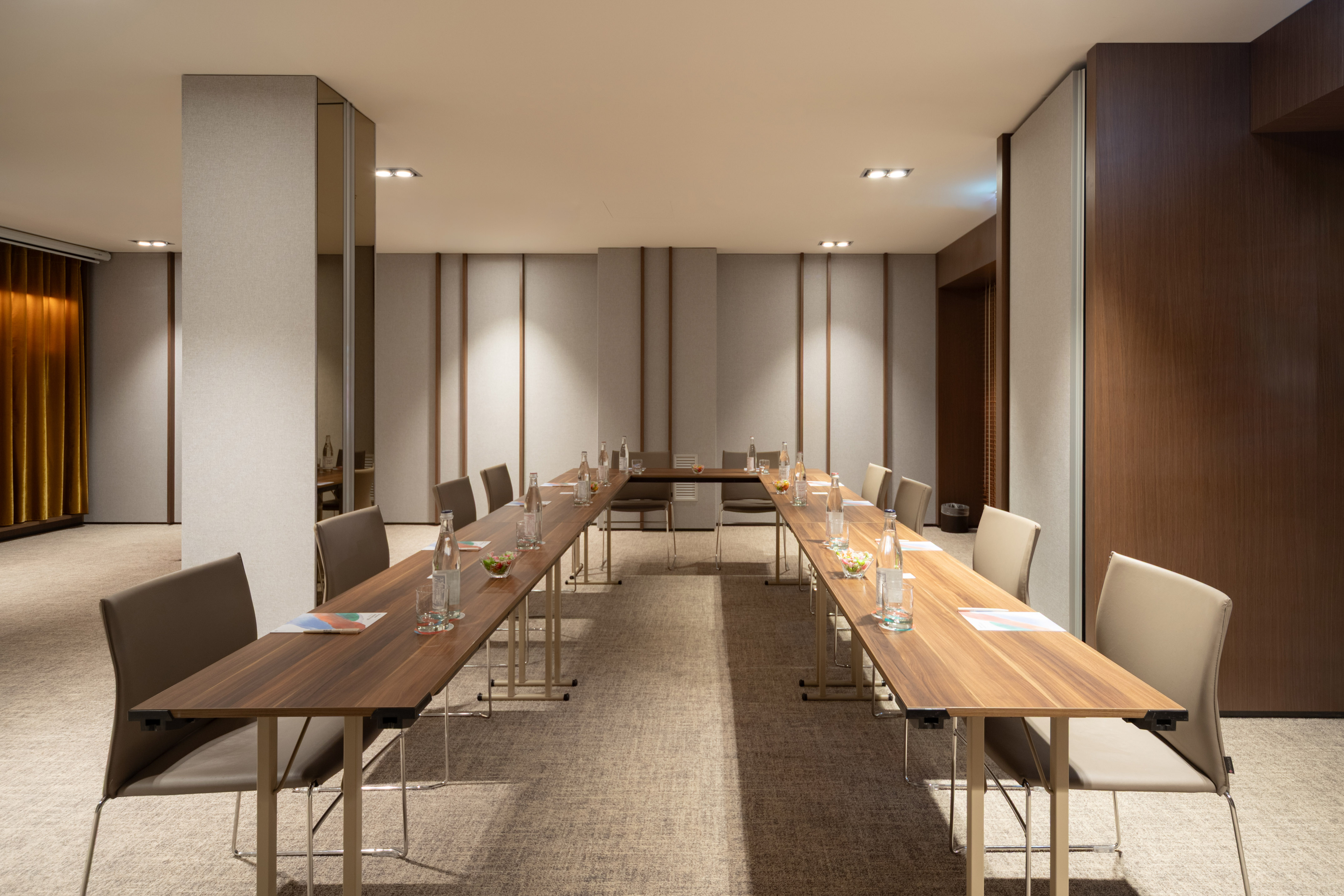 Modern U-shaped meeting room setup with tables, chairs, and refreshments.