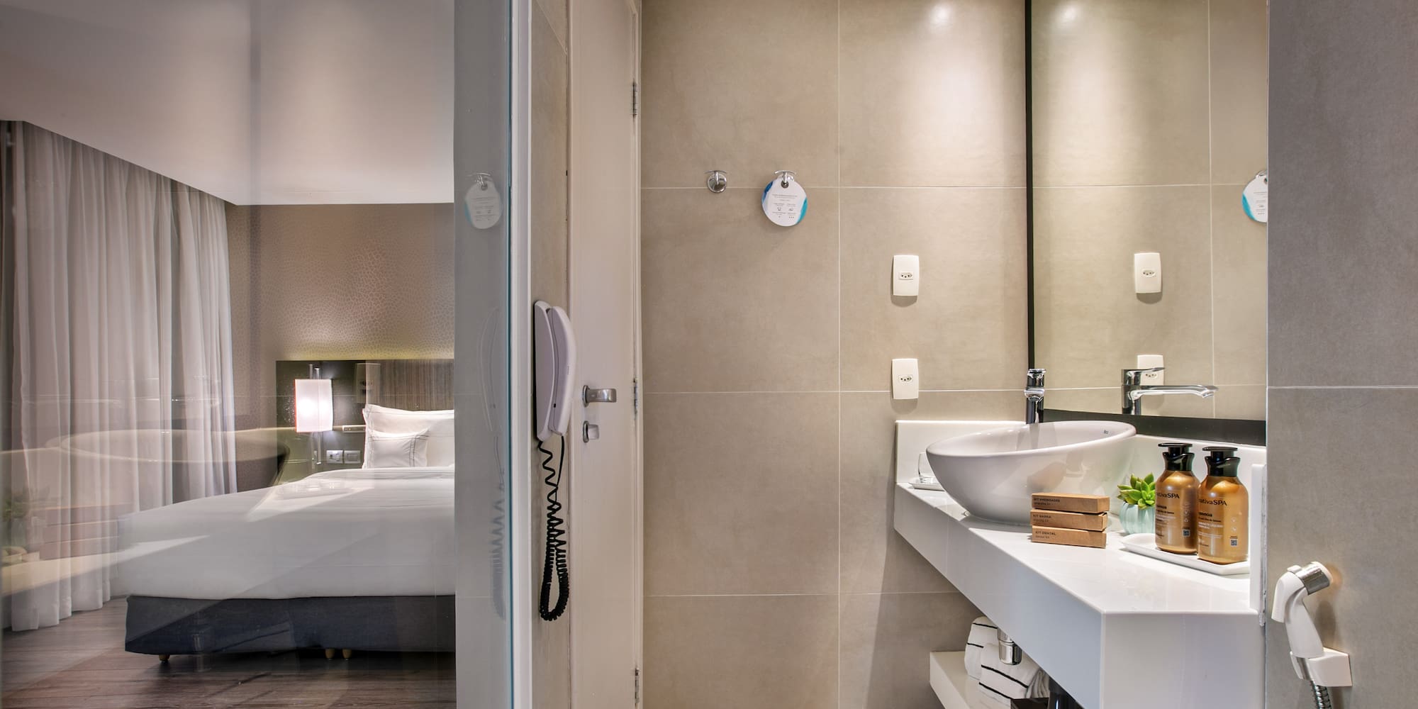 Sleek hotel bathroom with vanity and glass partition overlooking the bedroom.
