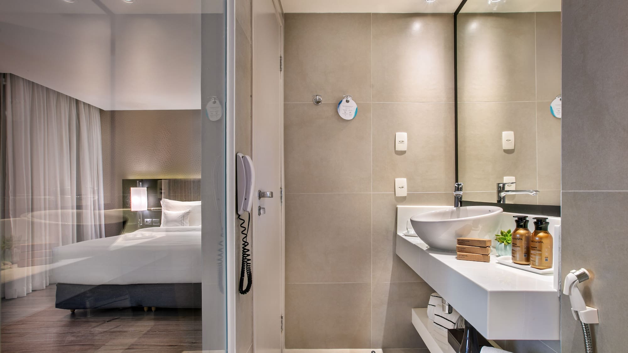 Sleek hotel bathroom with vanity and glass partition overlooking the bedroom.