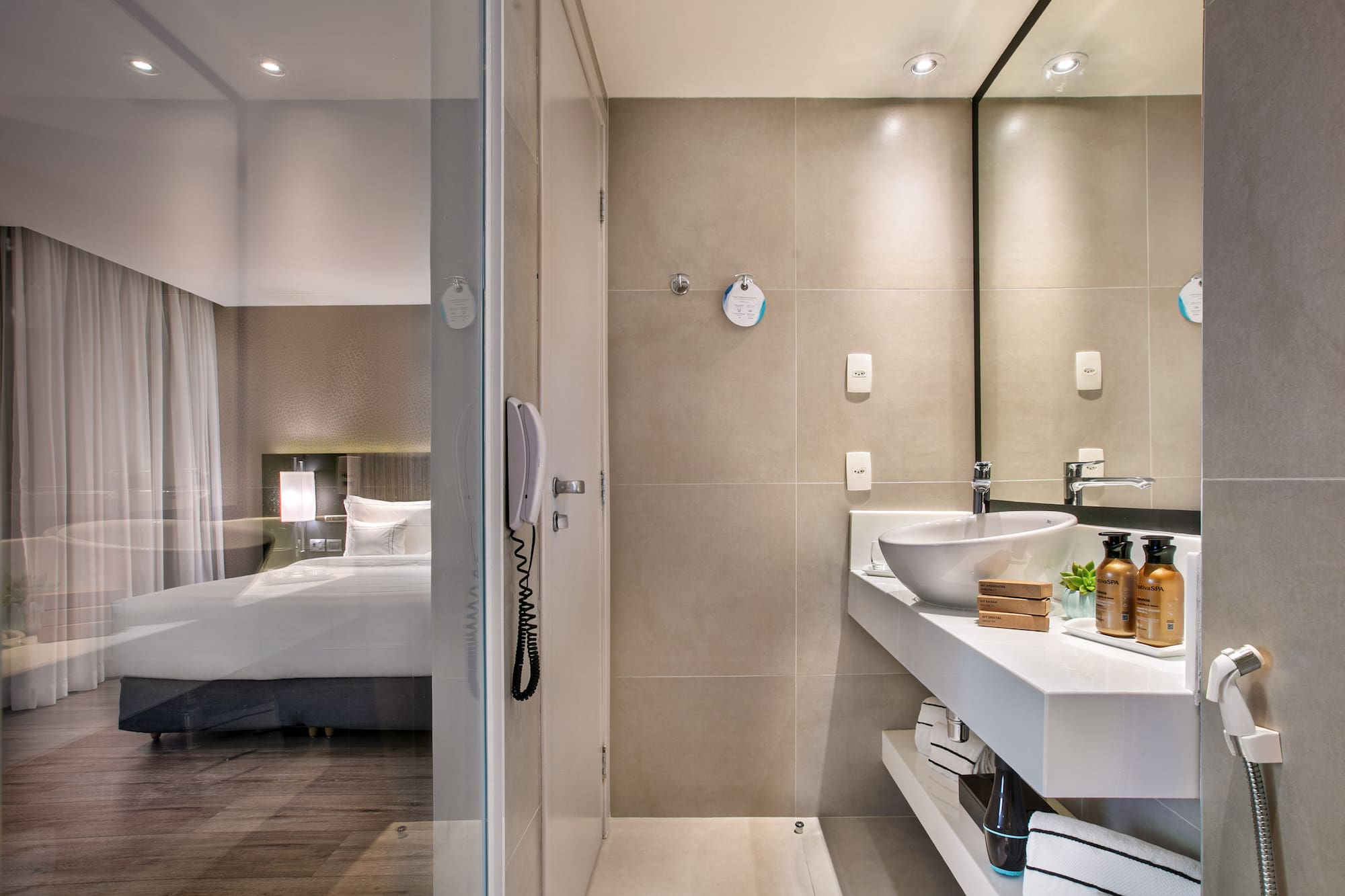 Sleek hotel bathroom with vanity and glass partition overlooking the bedroom.