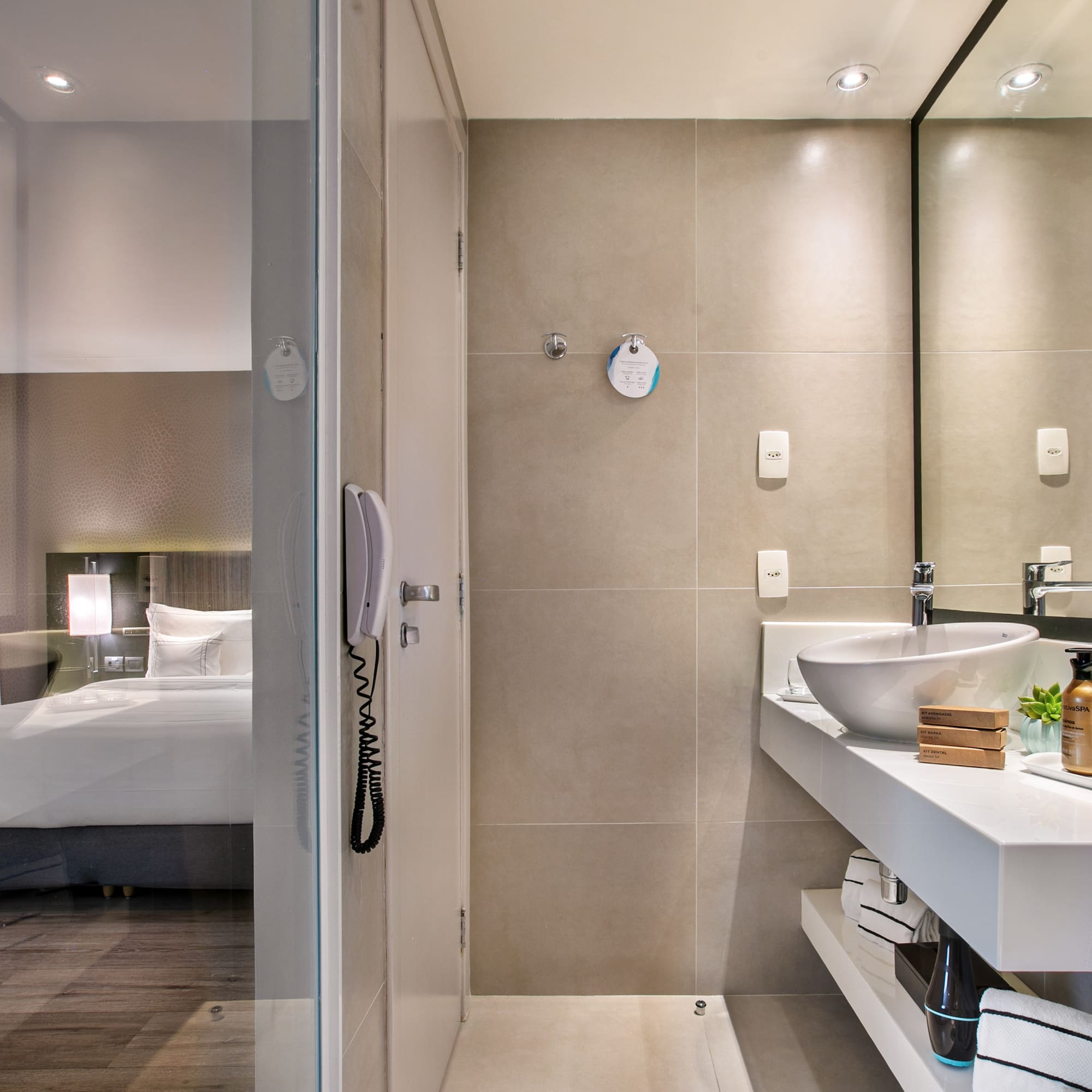 Sleek hotel bathroom with vanity and glass partition overlooking the bedroom.