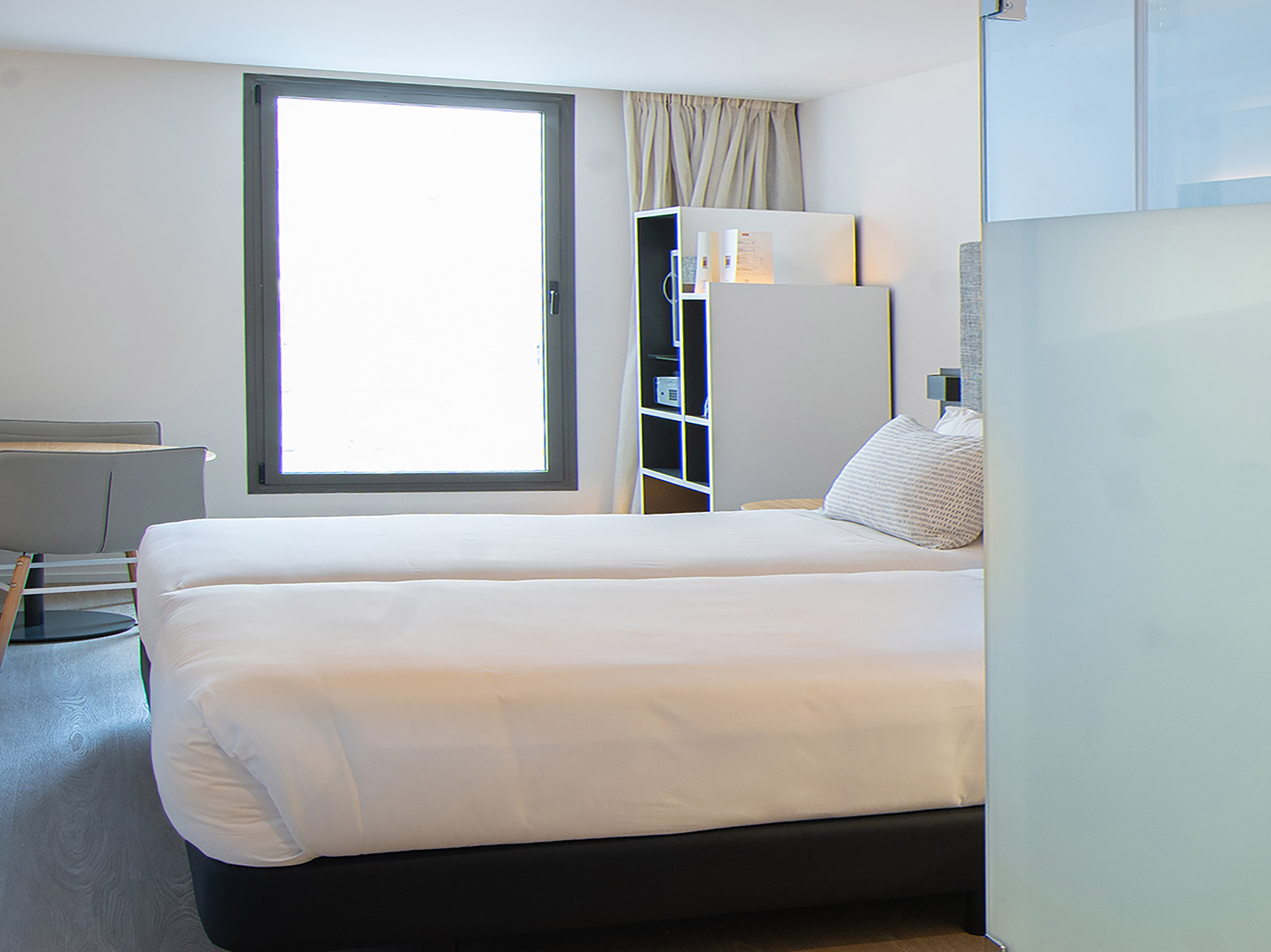Modern hotel room with twin beds, bright window, and neutral decor.
