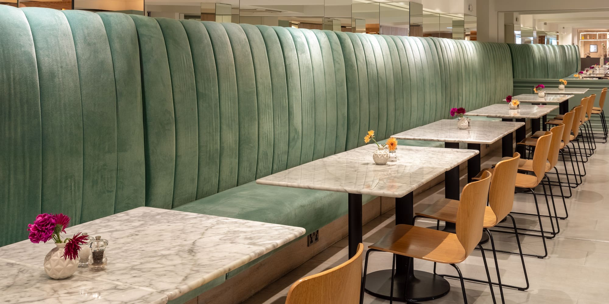 Green velvet banquette and marble tables in a modern cafe or hotel dining room.