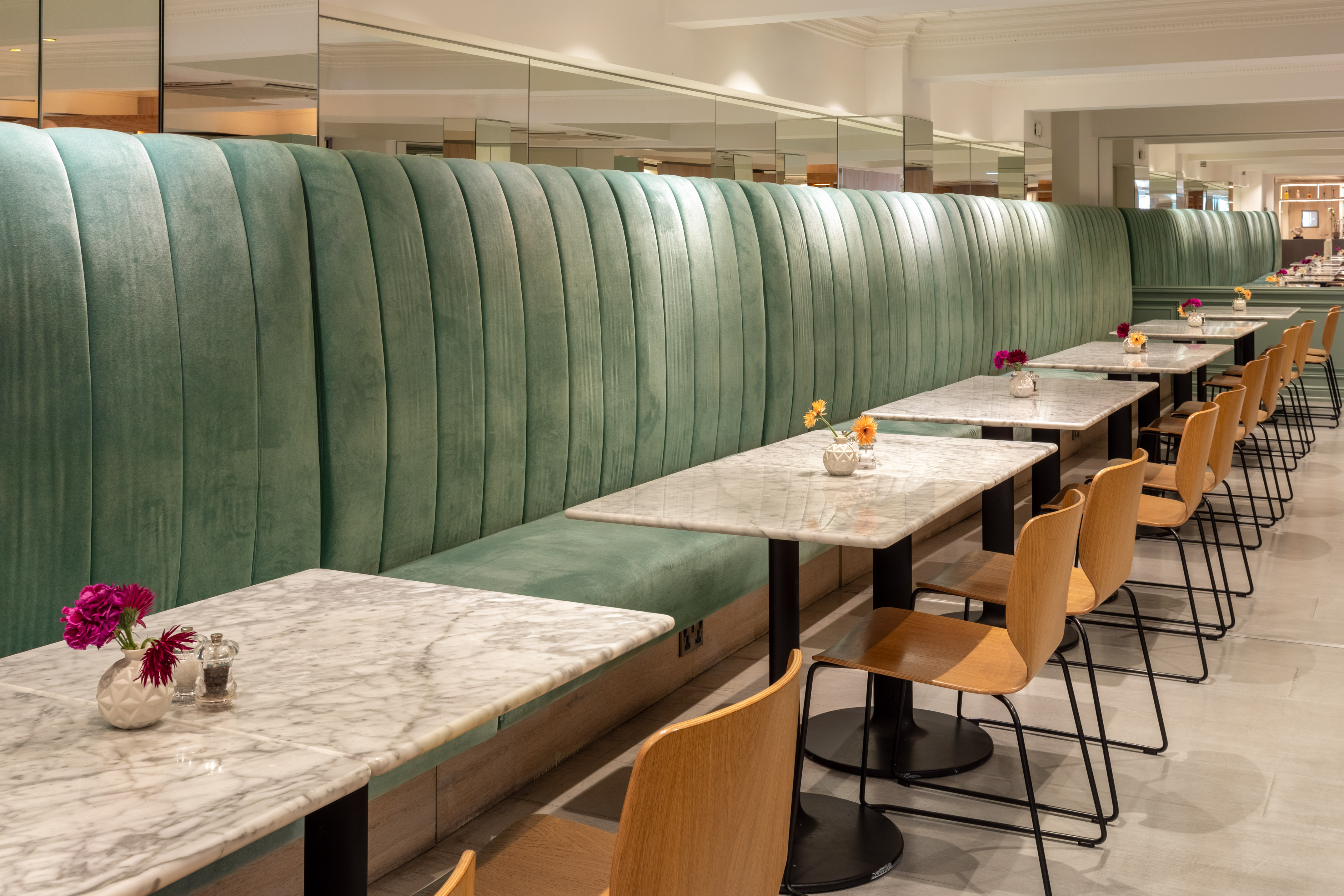 Green velvet banquette and marble tables in a modern cafe or hotel dining room.