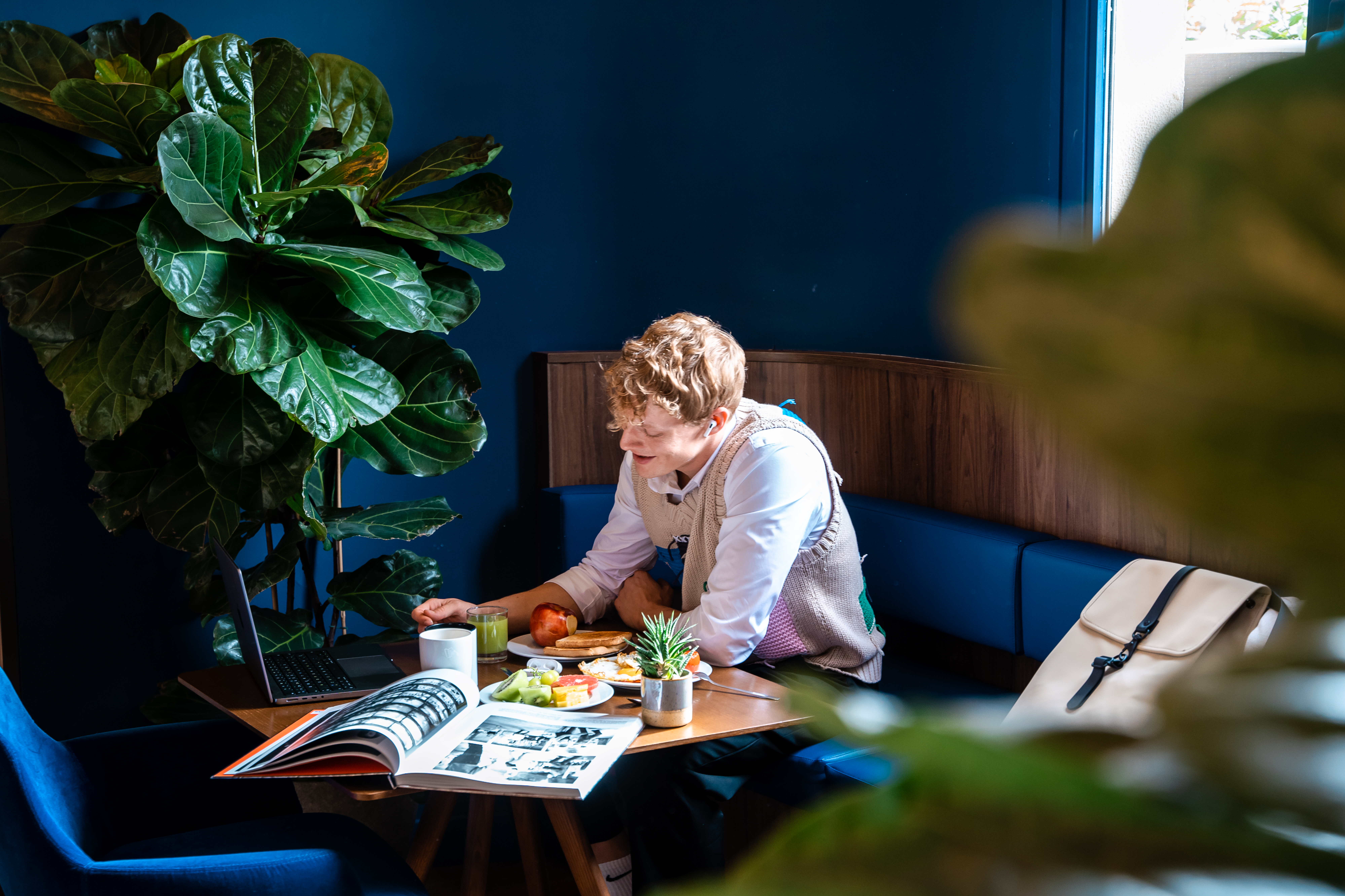 A woman sits at a table, with a laptop and some food in front of her.