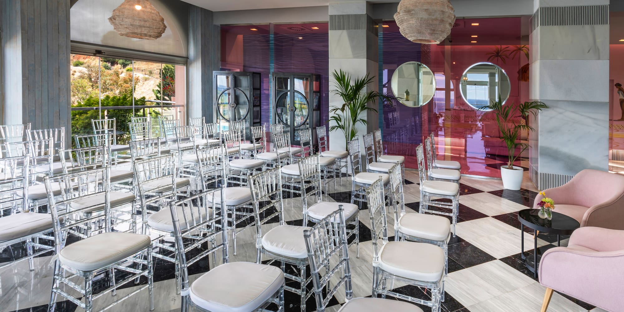 Modern event space with clear chairs, checkered floor, and scenic outdoor view.