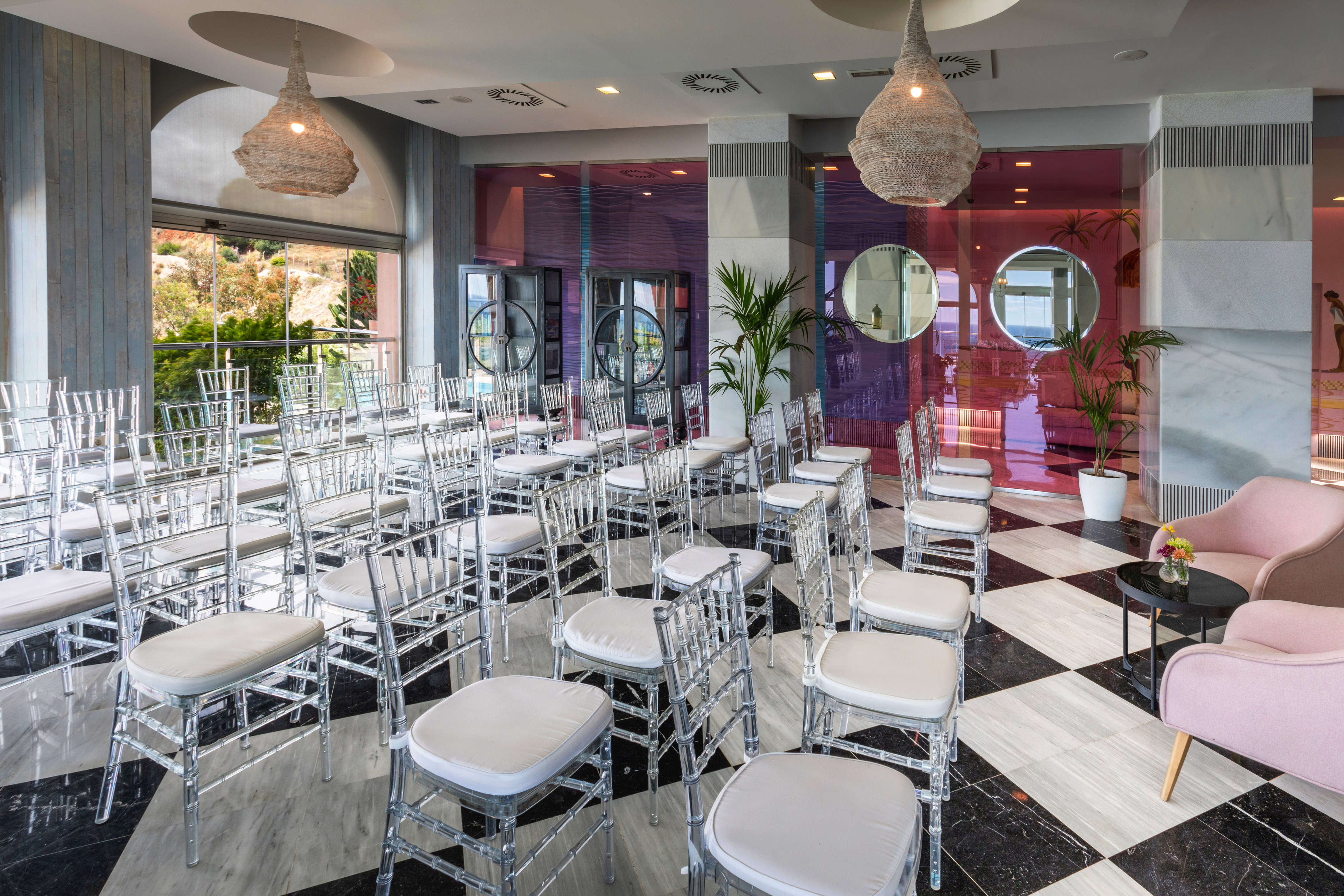 Modern event space with clear chairs, checkered floor, and scenic outdoor view.