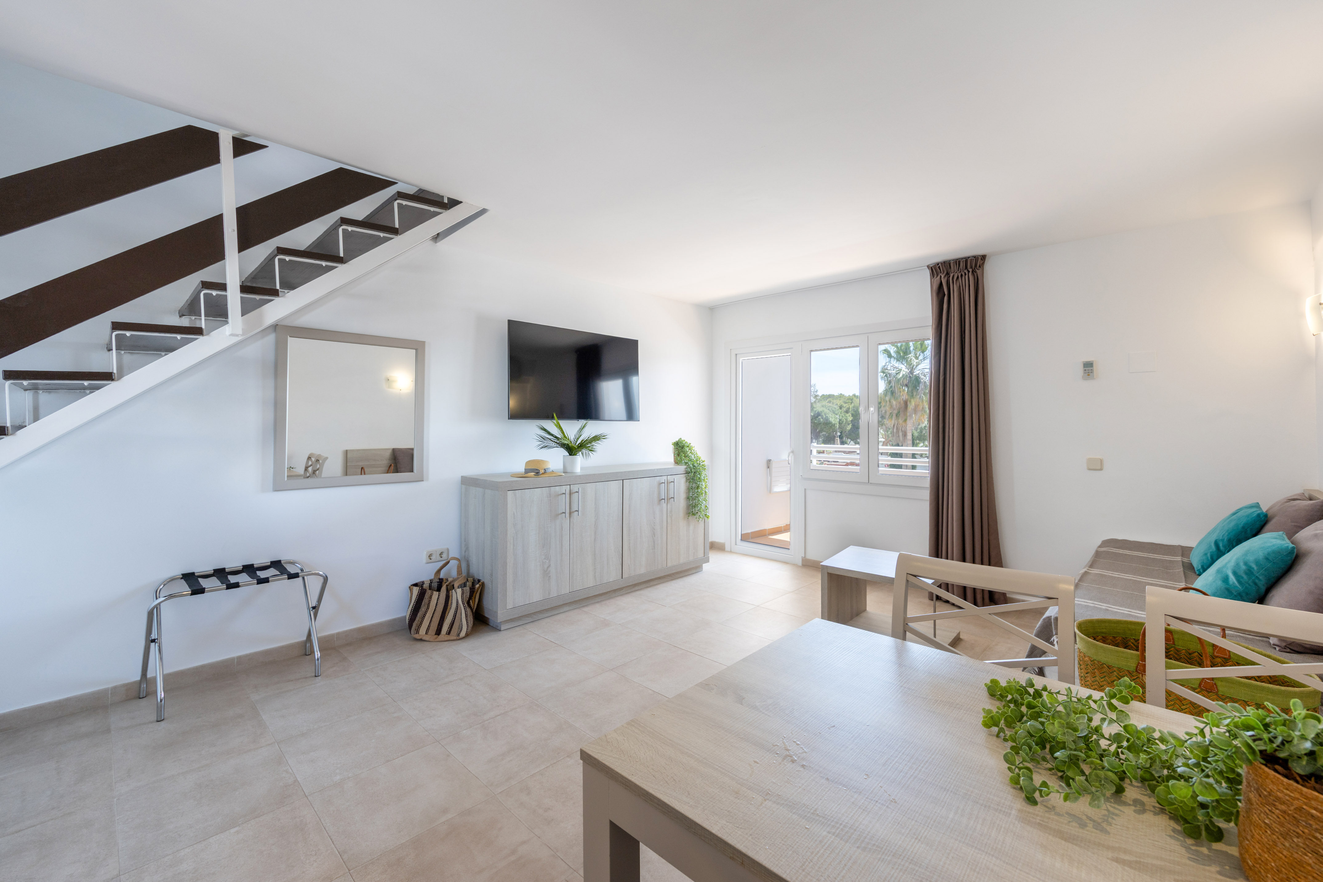Modern open-plan apartment living room with staircase, TV, dining, and balcony.