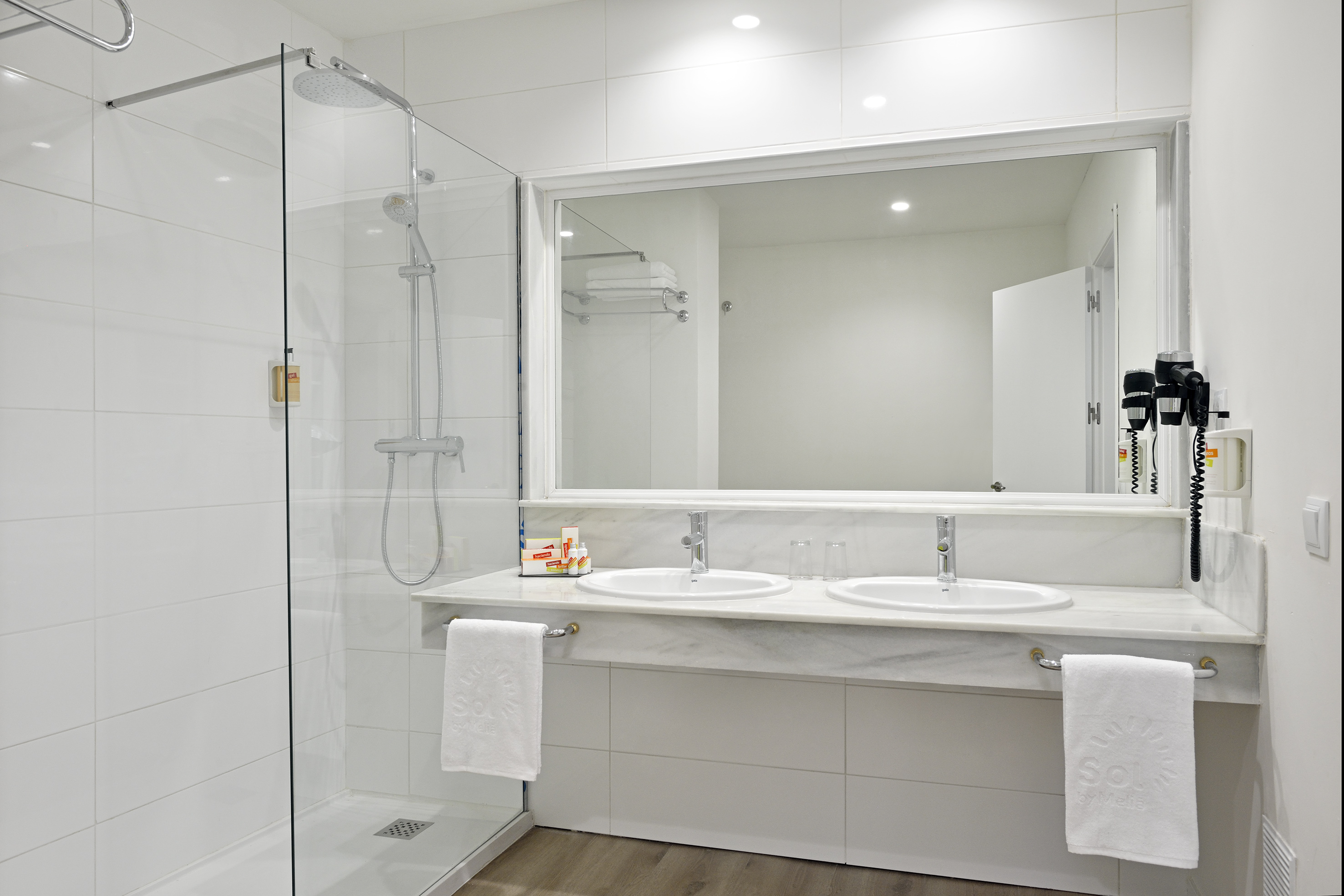 Modern hotel bathroom with walk-in shower, double vanity, and mirror.