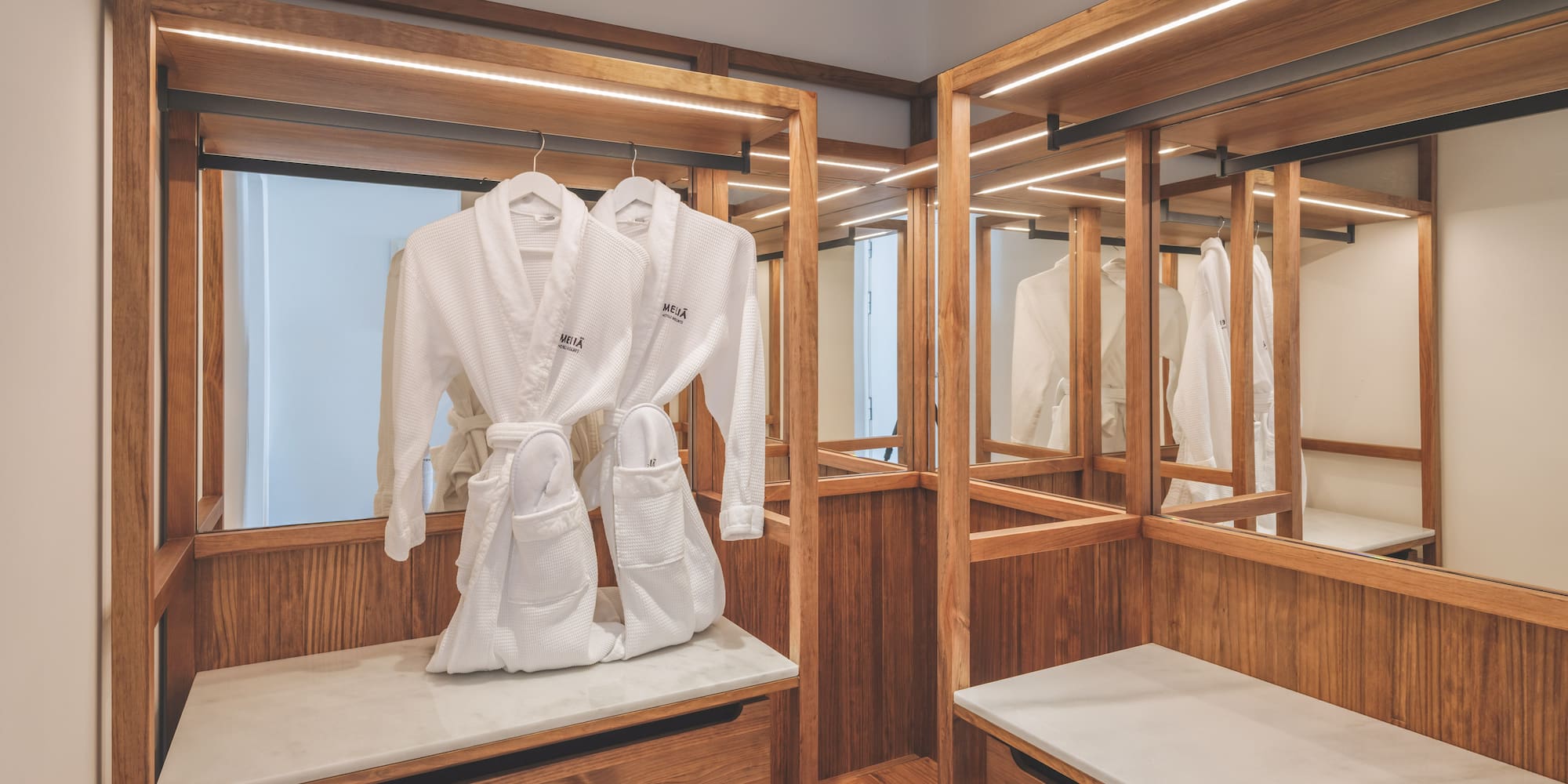 Modern hotel closet with wooden accents, LED lights, and white bathrobes.