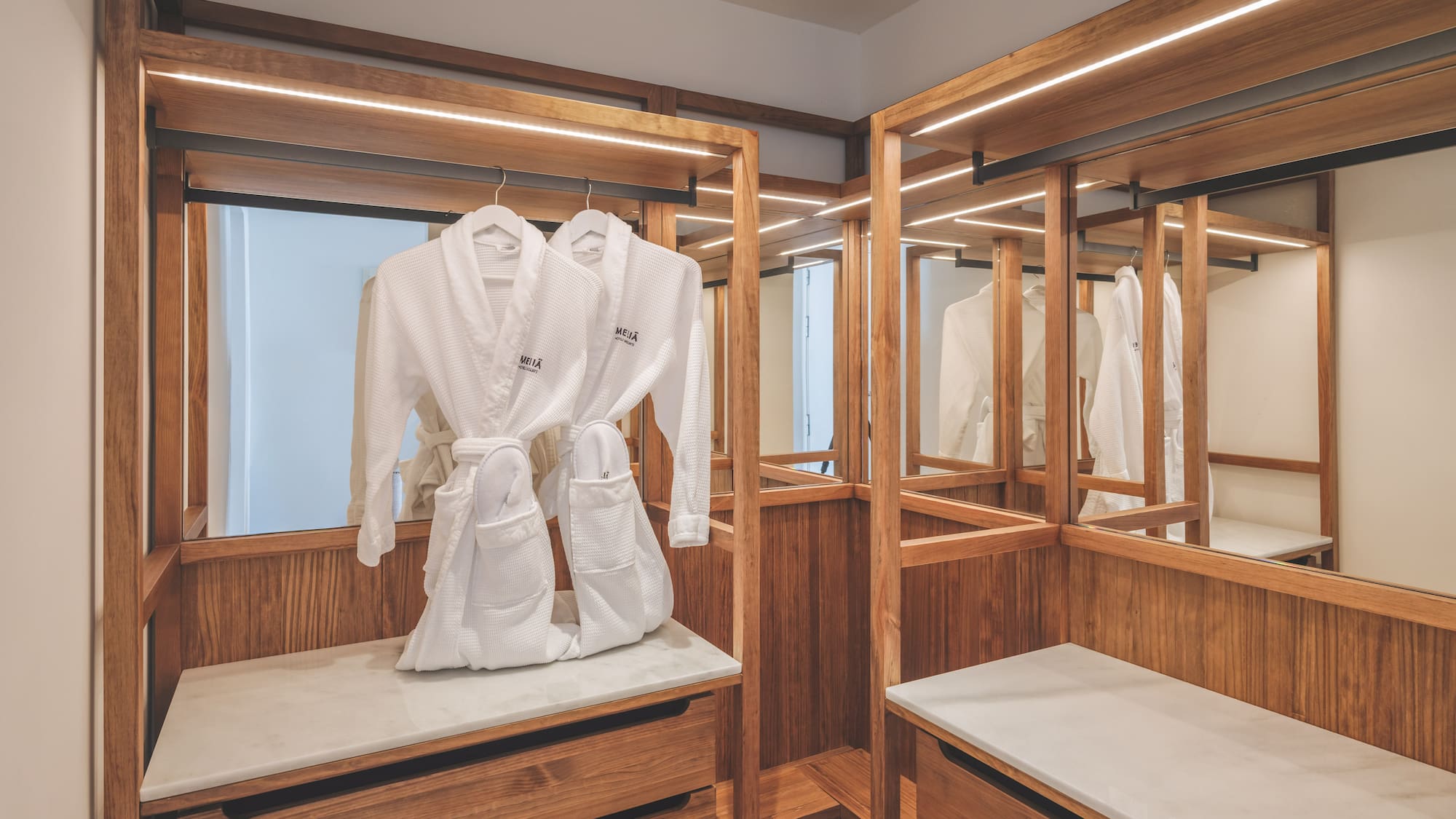 Modern hotel closet with wooden accents, LED lights, and white bathrobes.