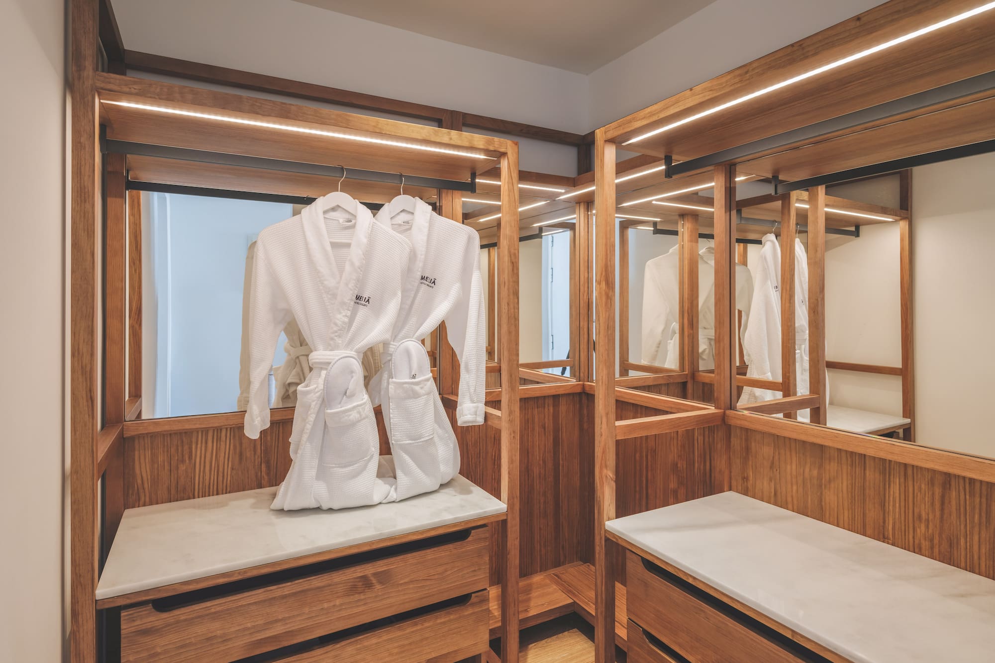 Modern hotel closet with wooden accents, LED lights, and white bathrobes.