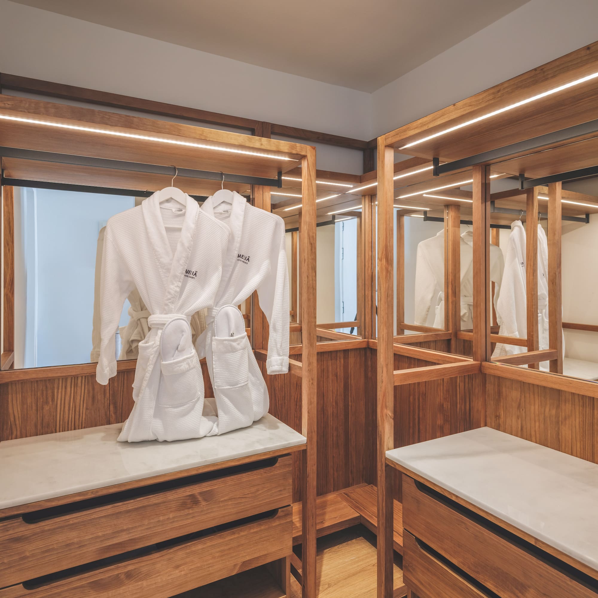 Modern hotel closet with wooden accents, LED lights, and white bathrobes.