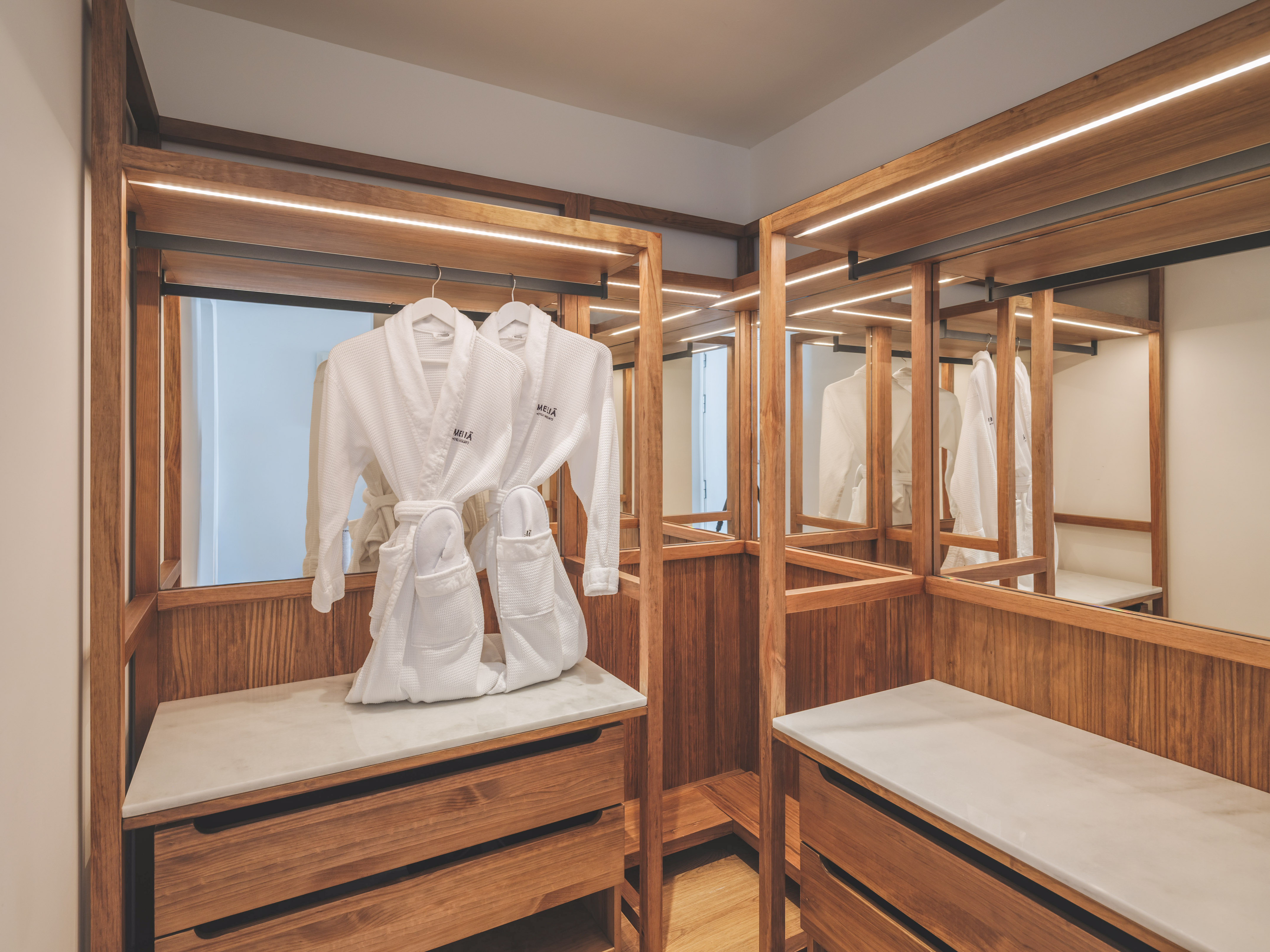 Modern hotel closet with wooden accents, LED lights, and white bathrobes.