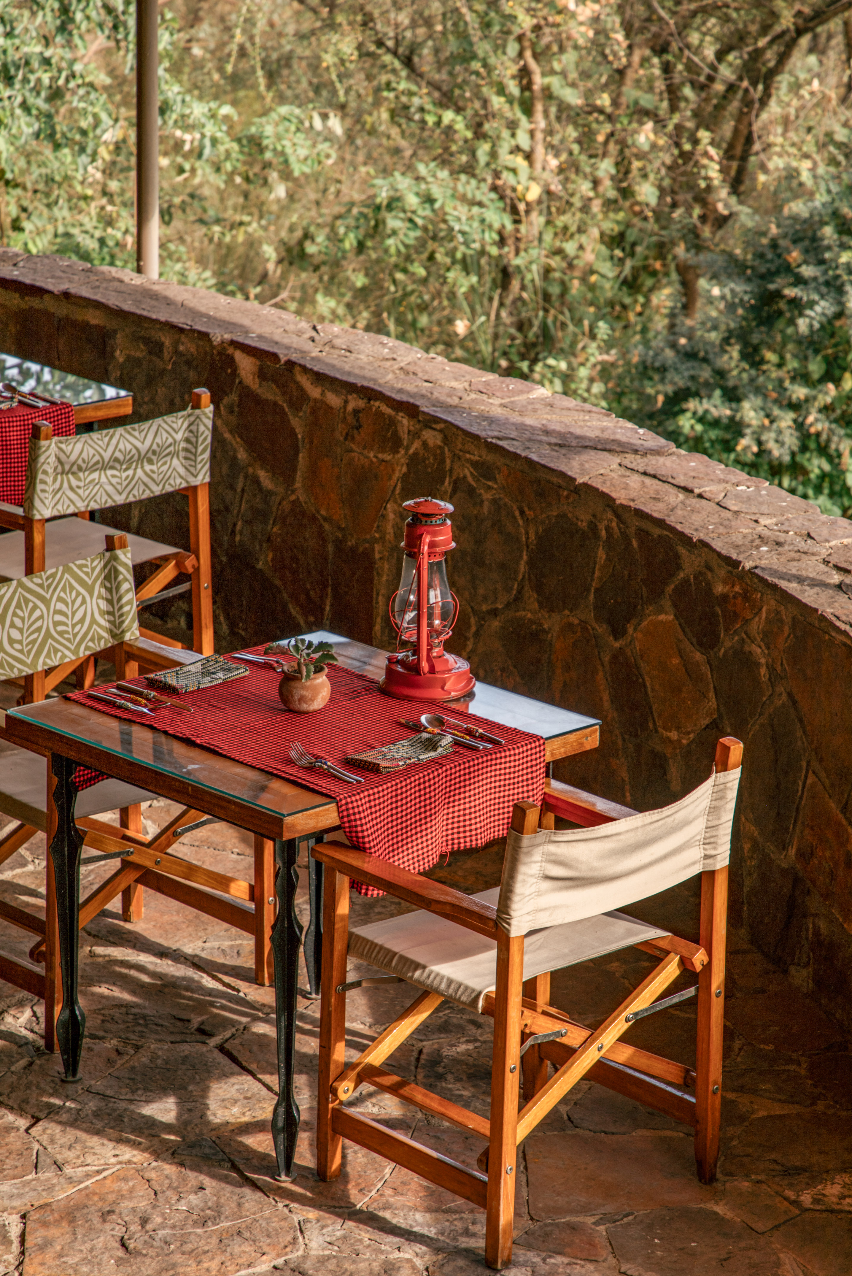 Set outdoor dining table with red lantern, safari chairs, and green nature view.