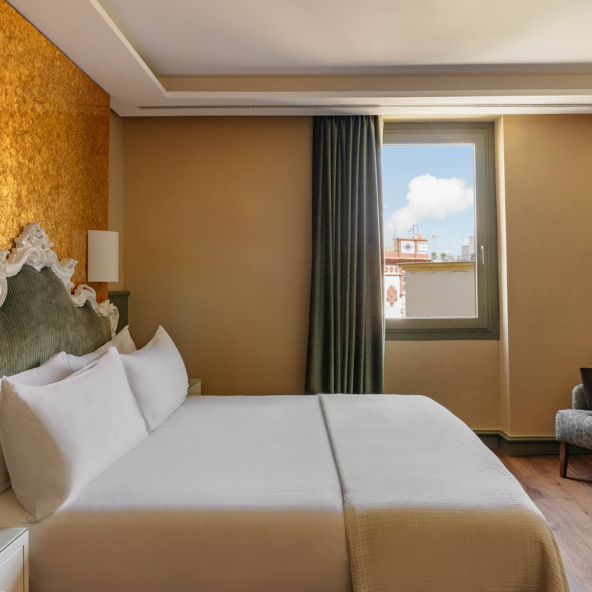 Dormitorio elegante de hotel con cama, cabecero clásico, pared dorada y ventana.