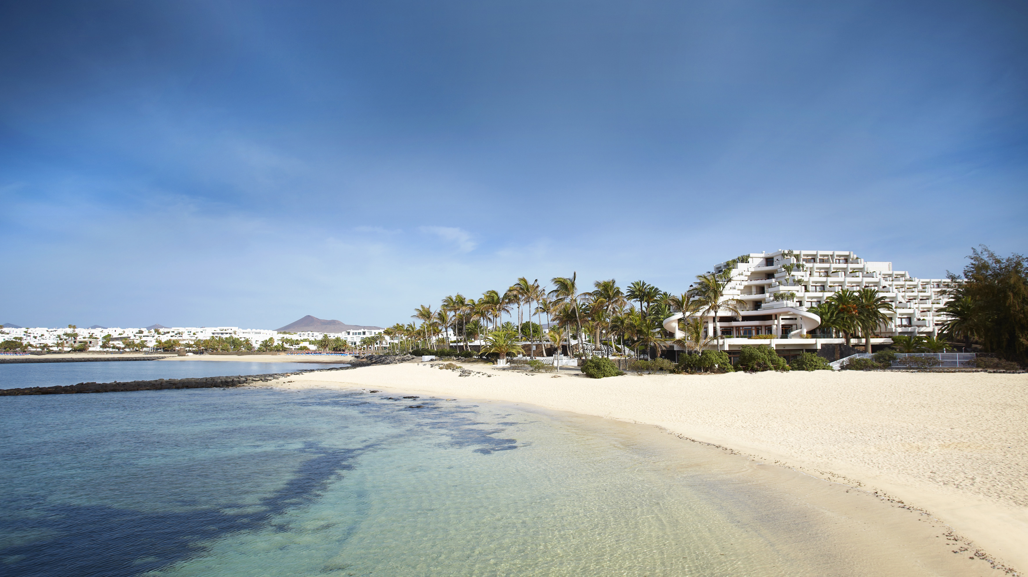 Beachfront resort with white sand, clear blue water, and palm trees.