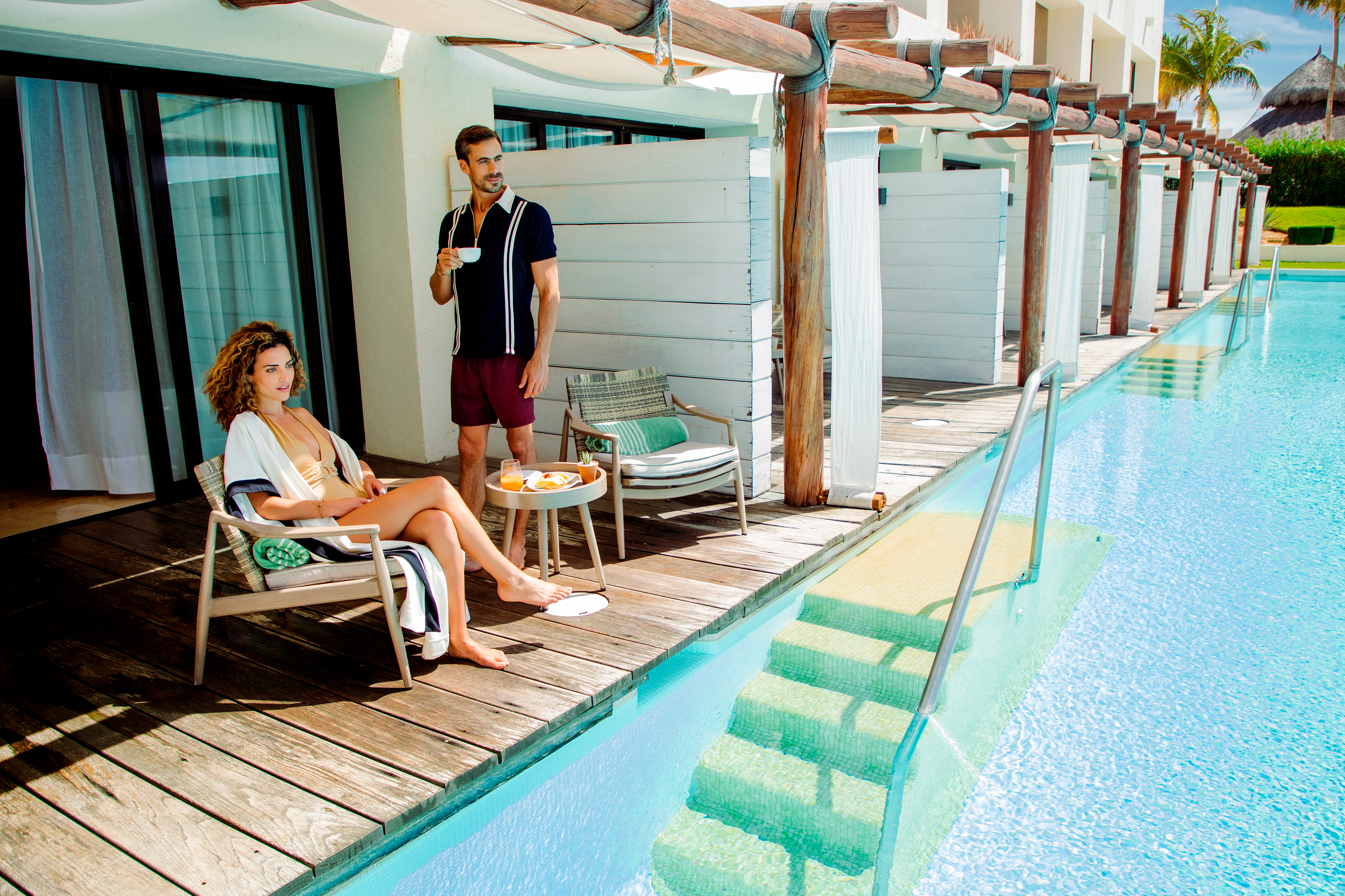 a man and woman sitting on a deck by a pool