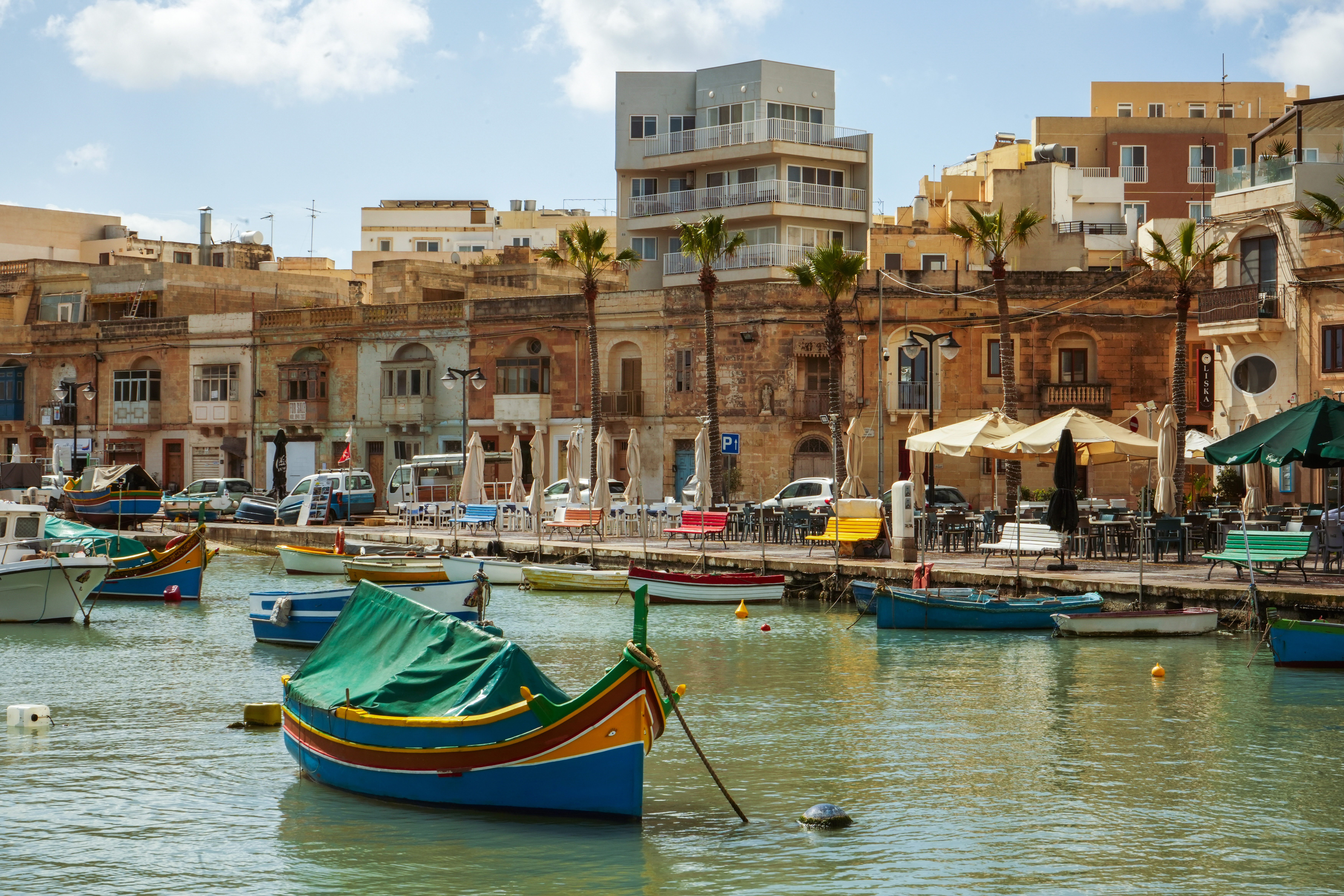 Colorful Maltese luzzu boats in a sunny harbor with historic waterfront buildings.