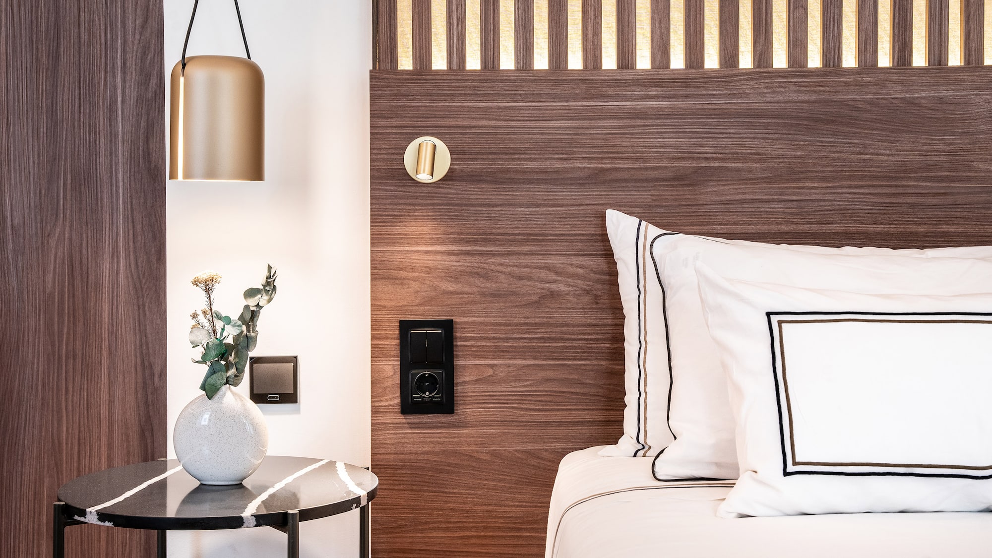a bed with white pillows and a vase of flowers on a table