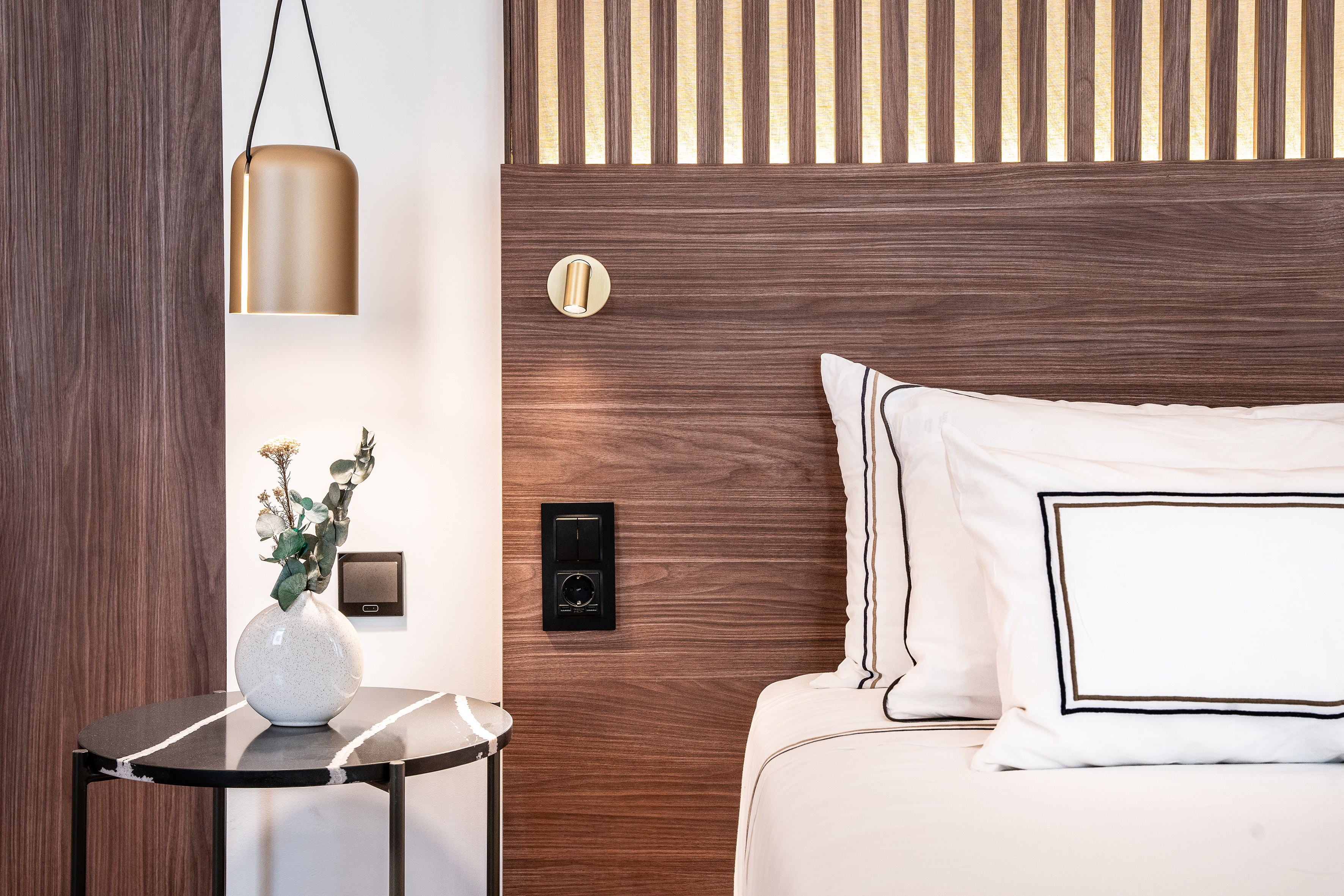 Modern bedroom: wood headboard, integrated lights, golden pendant, bedside table.