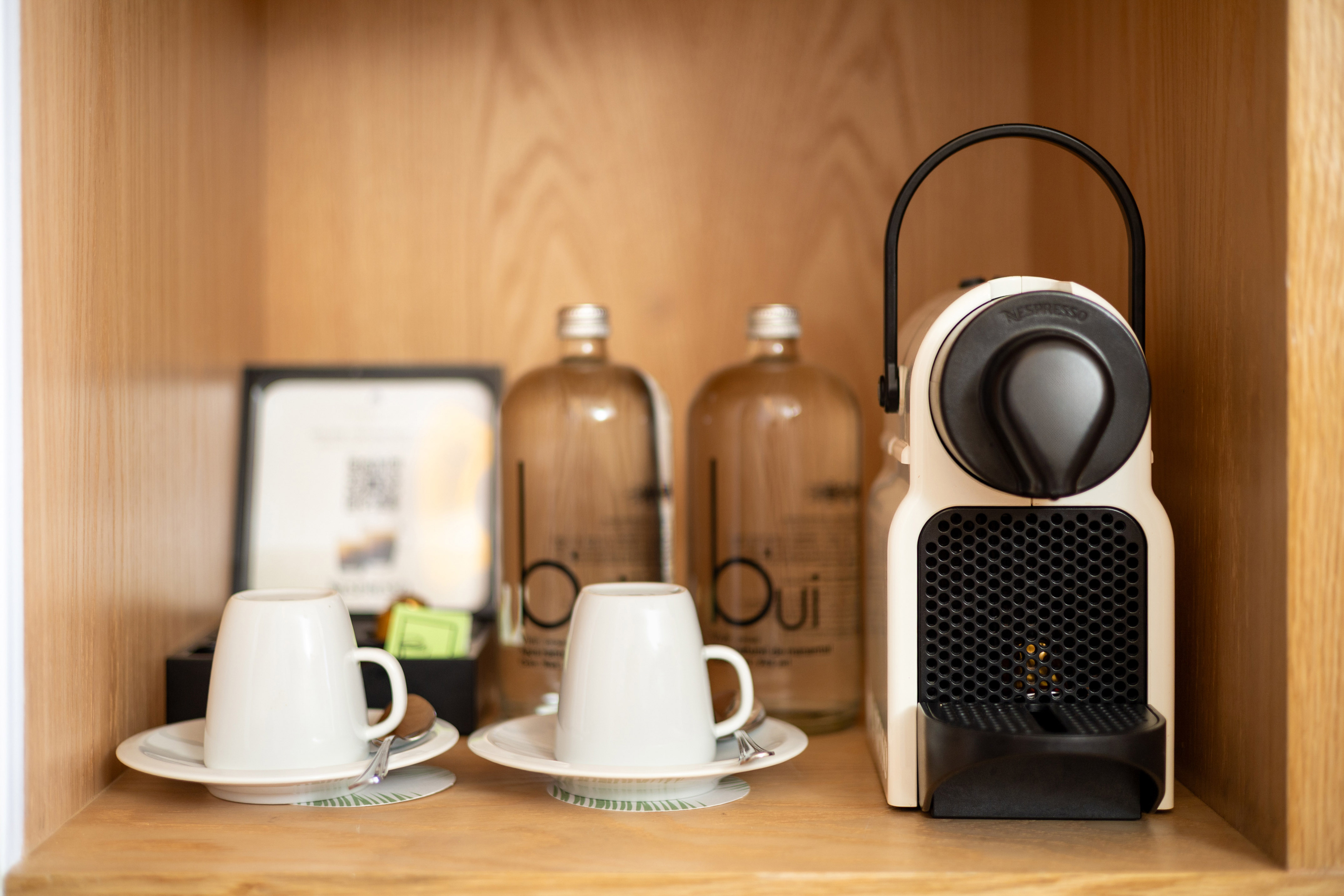 Nespresso machine, white cups, bottled water, hotel amenities on wooden shelf.