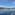Luxury grey yacht on sparkling blue sea with green wooded coast and clear sky.