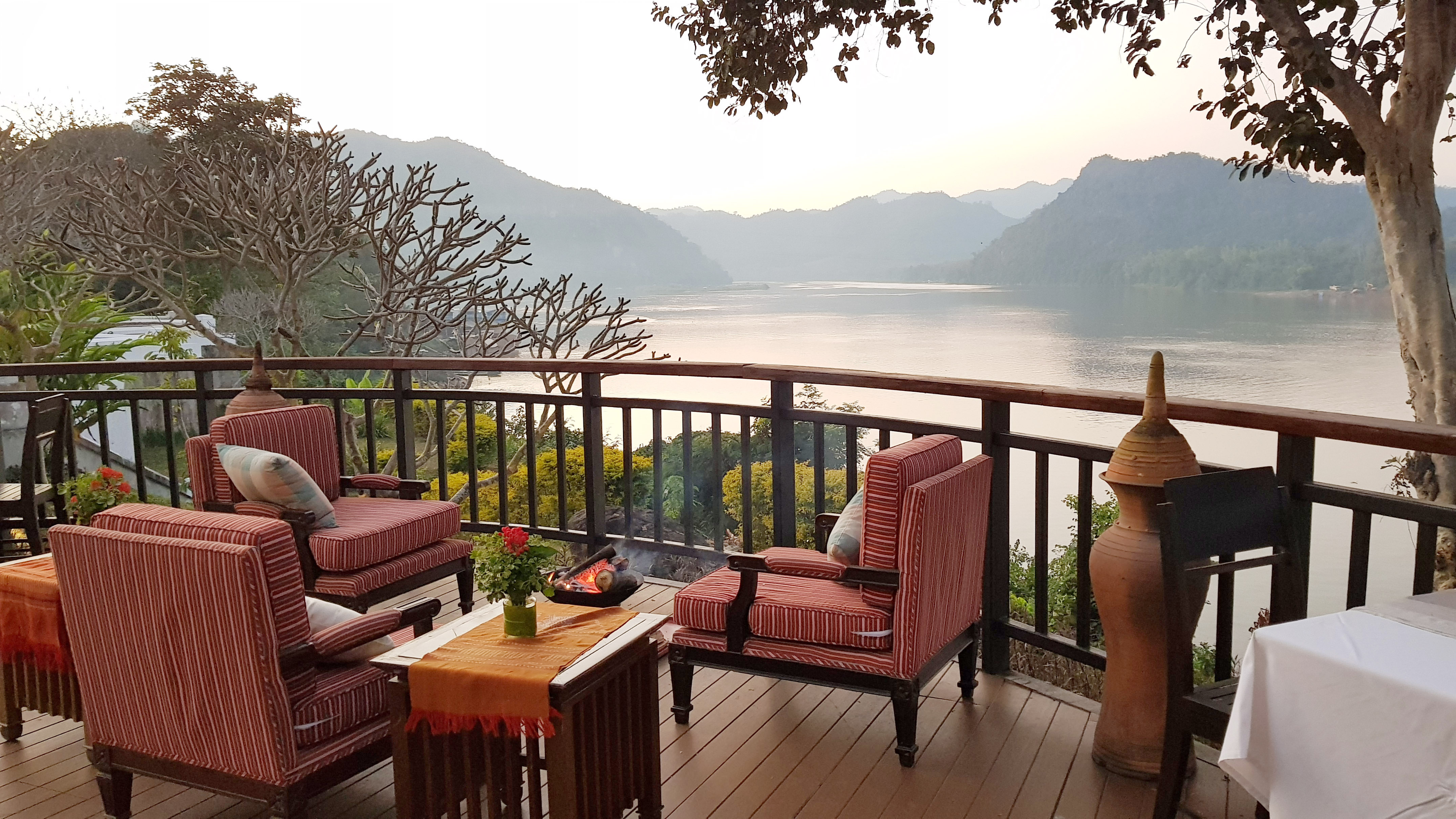 Cozy deck with red chairs, fire pit, overlooking a scenic river and mountains.