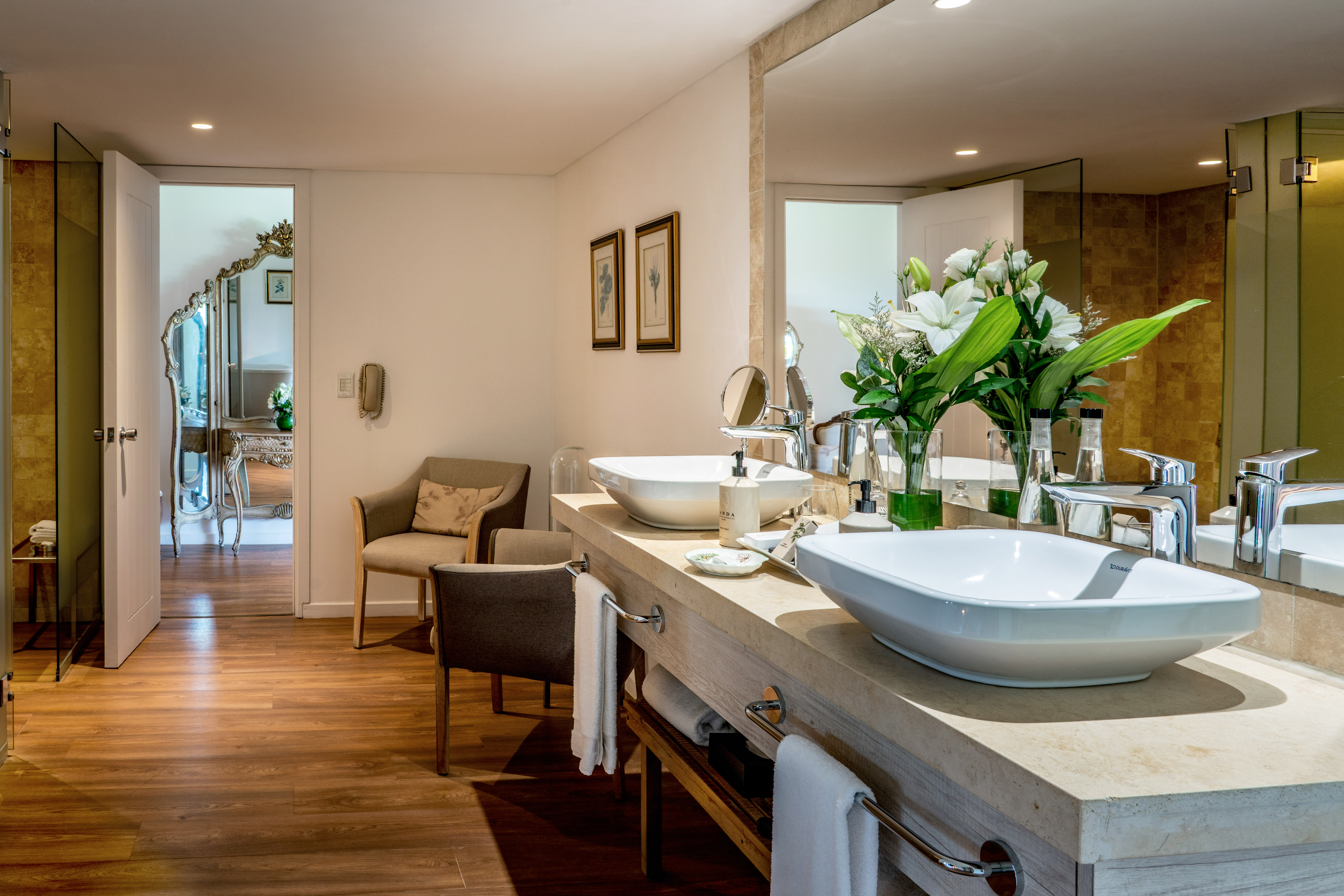 Modern hotel bathroom with double vessel sinks, large mirror, and wood floor.
