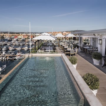 a pool with tables and chairs on a rooftop overlooking a harbor