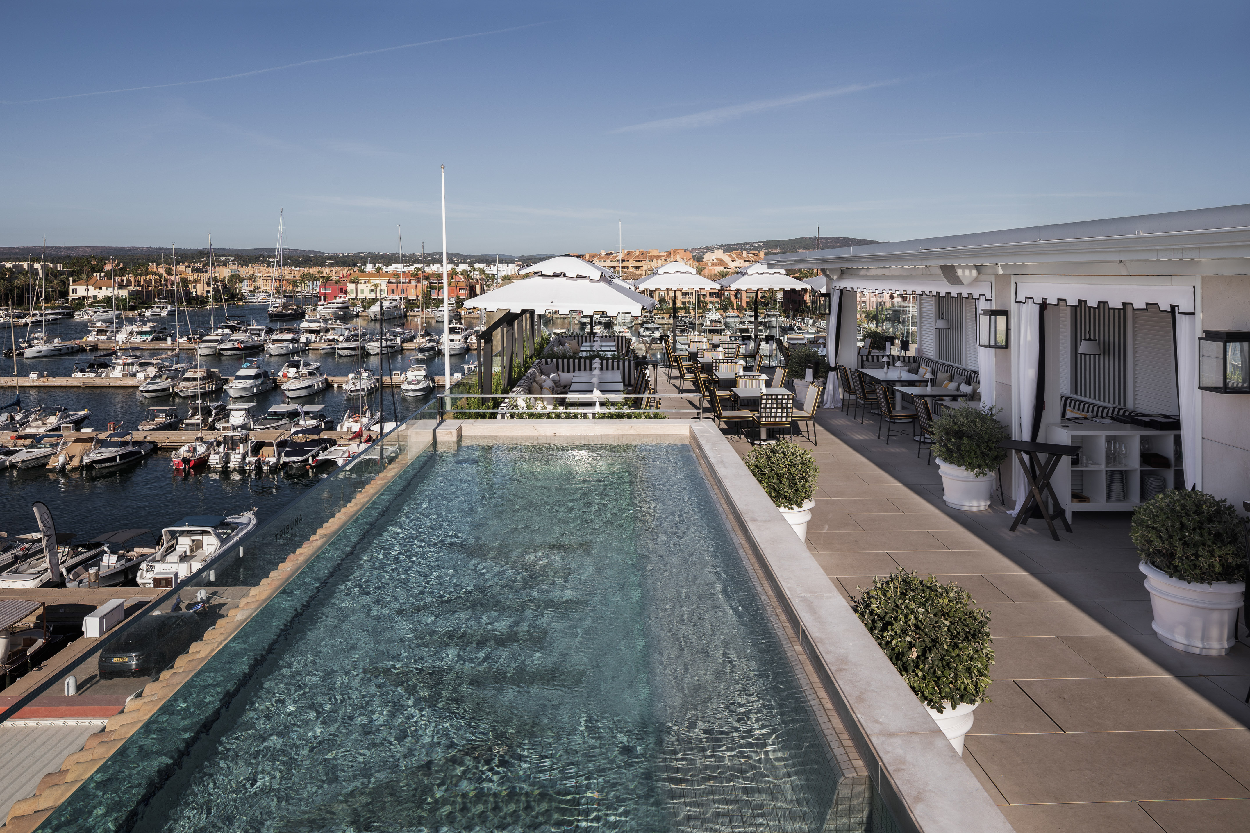 a pool with tables and chairs on a rooftop overlooking a harbor