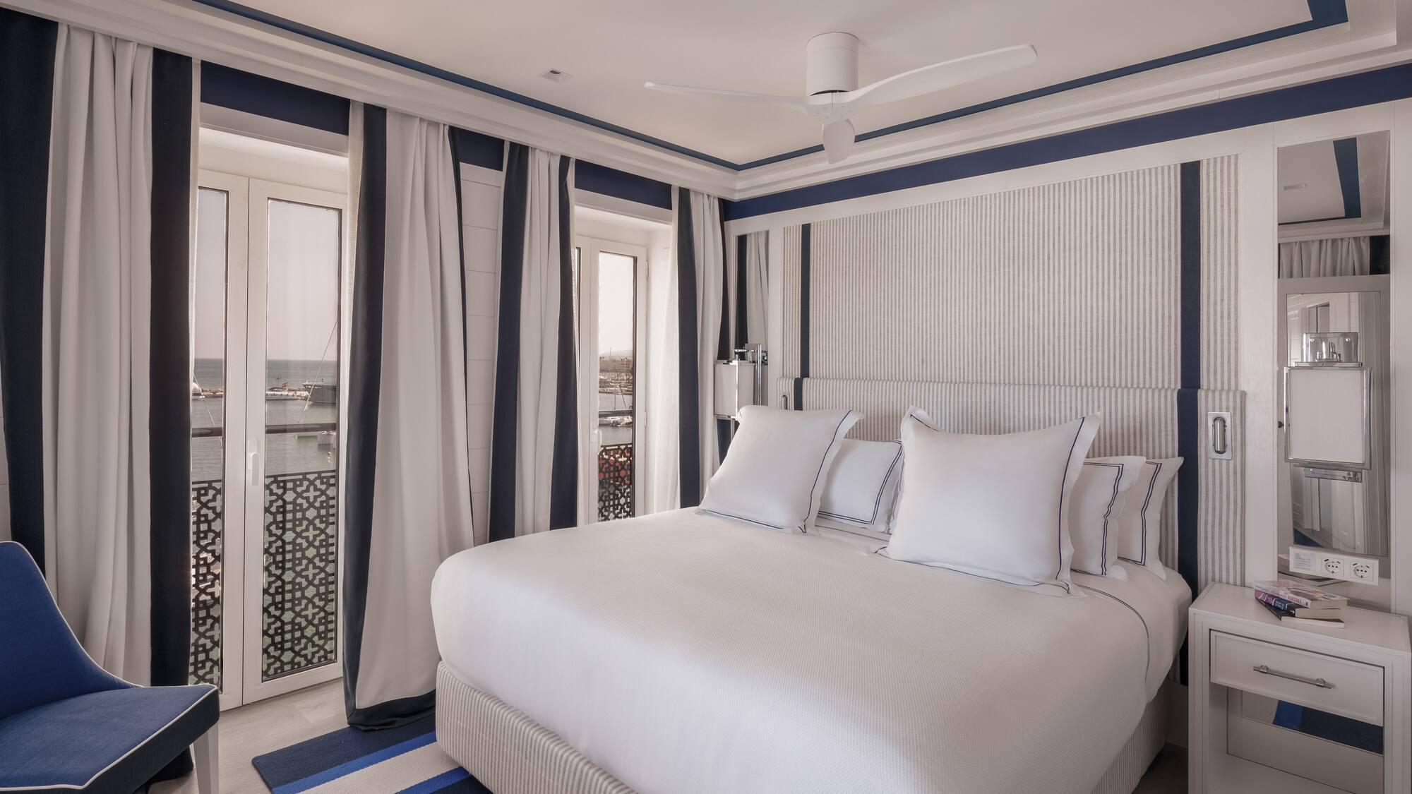 a bed with white pillows and a fan in a room with a window