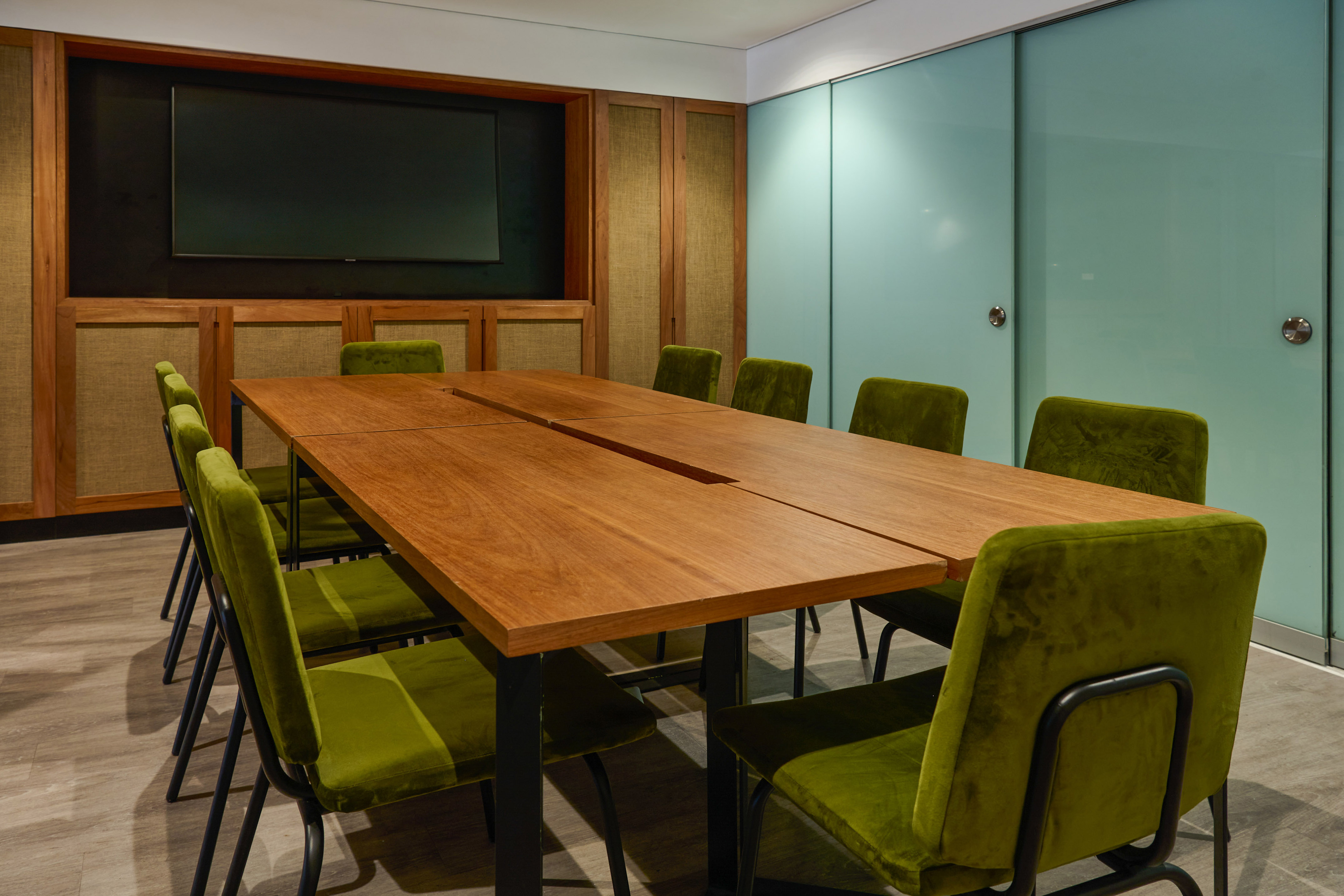 Modern meeting room with wooden conference table, green chairs, and wall TV.