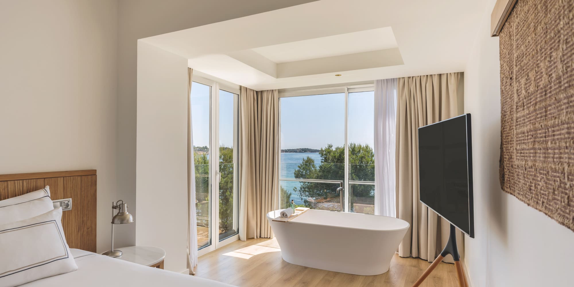 Modern hotel room with sea view, freestanding bathtub, and white bed.