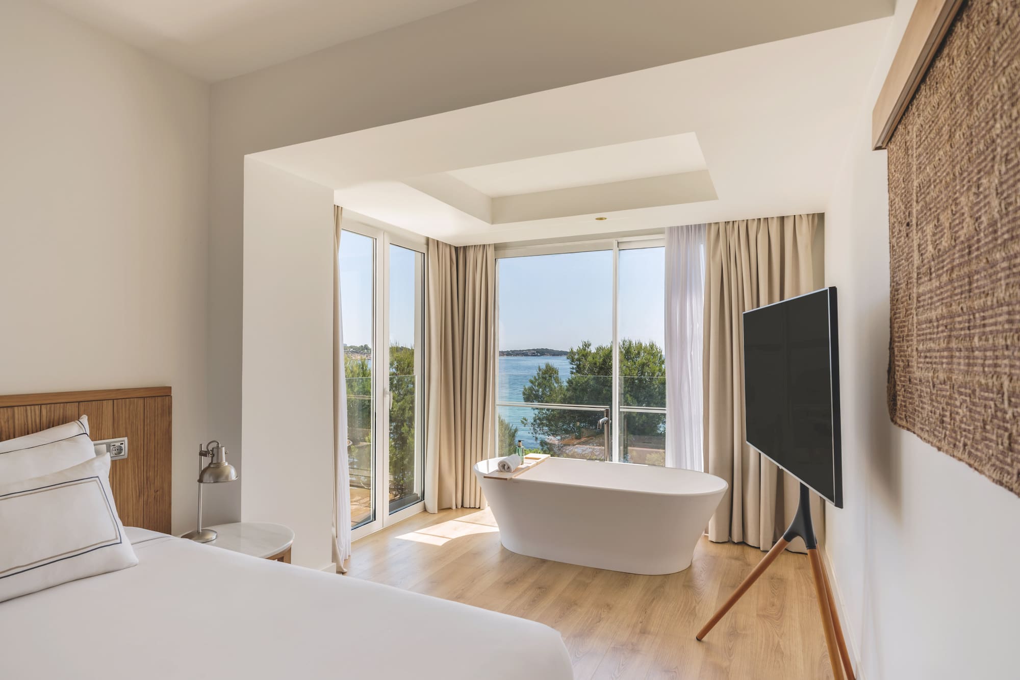 Modern hotel room with sea view, freestanding bathtub, and white bed.